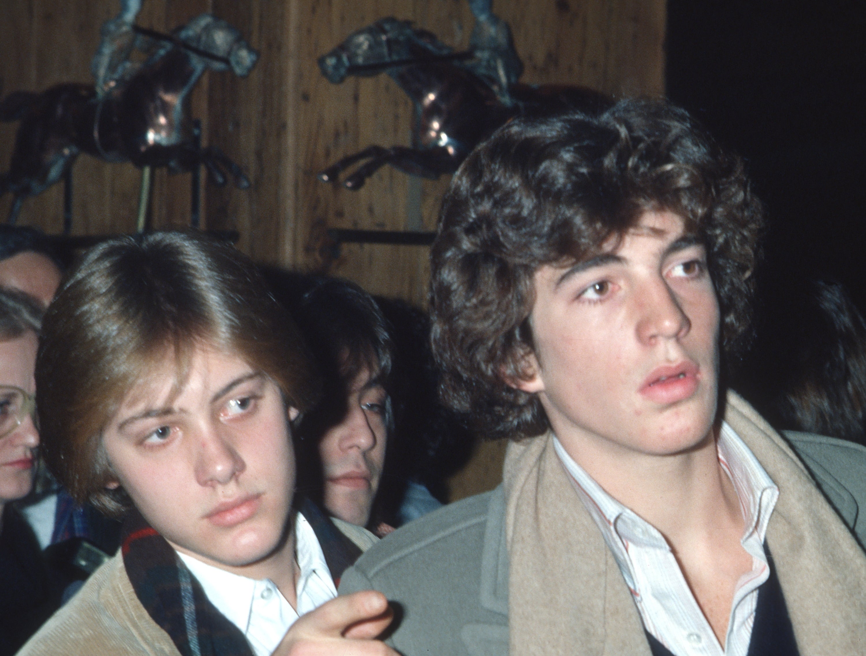 Two young men successful  1970s-style casual deterioration  are attending an event, with equine  sculptures successful  the background