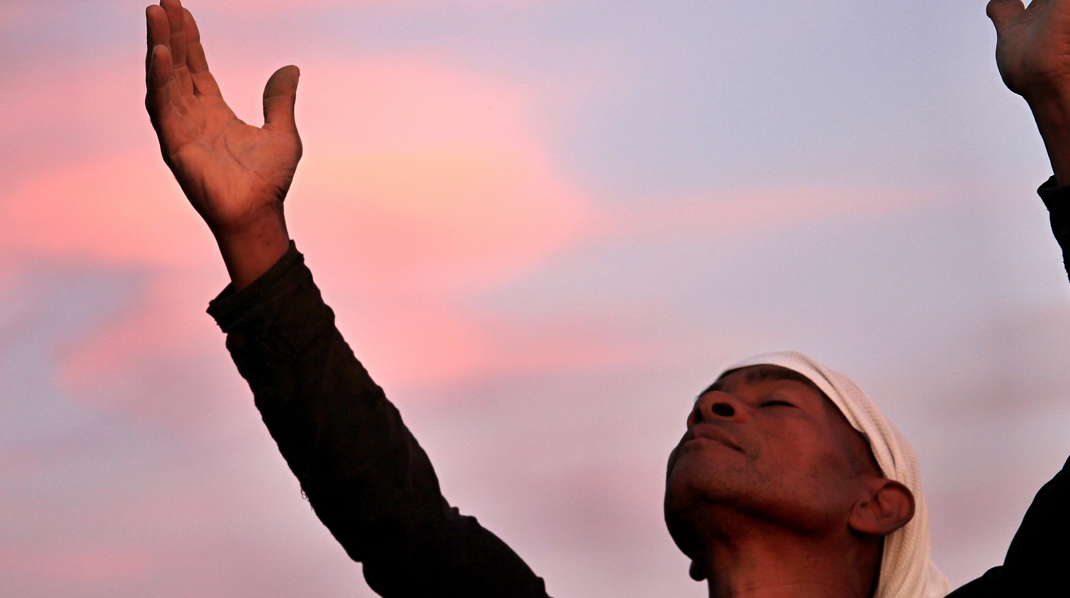 Person raising arms toward the entity  with eyes closed, wearing a long-sleeve garment  and headscarf, acceptable   against a brushed  entity  background