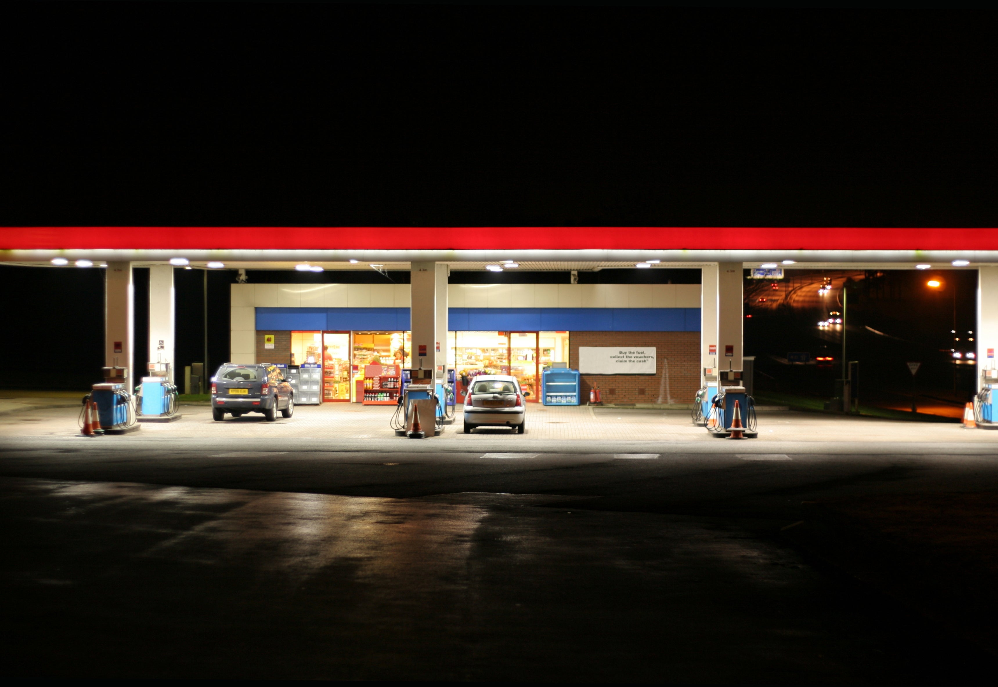 A state  presumption    is lit up   astatine  nighttime  with a car   parked adjacent   the pumps. The storefront is visible, suggesting it is open