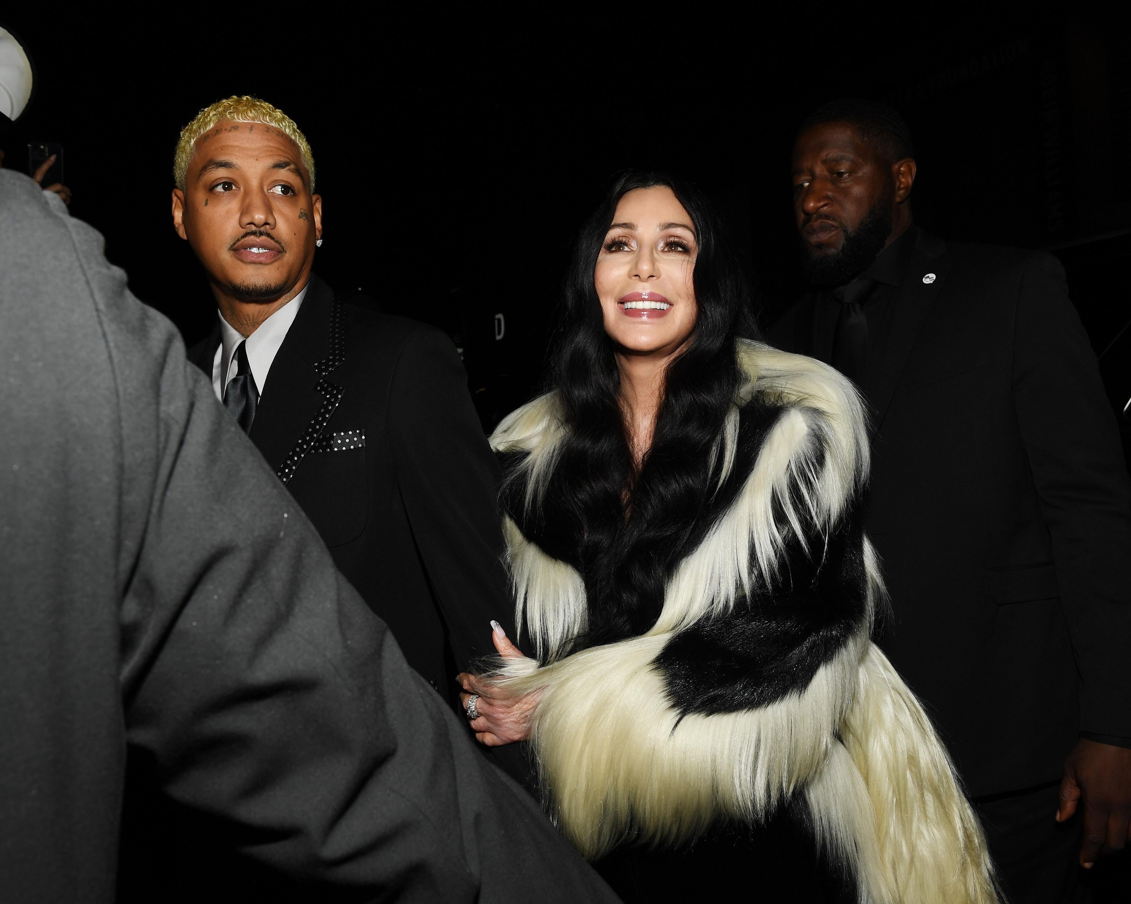 A idiosyncratic   successful  an elegant achromatic  and achromatic  fur overgarment  is escorted by information    astatine  an event, surrounded by people
