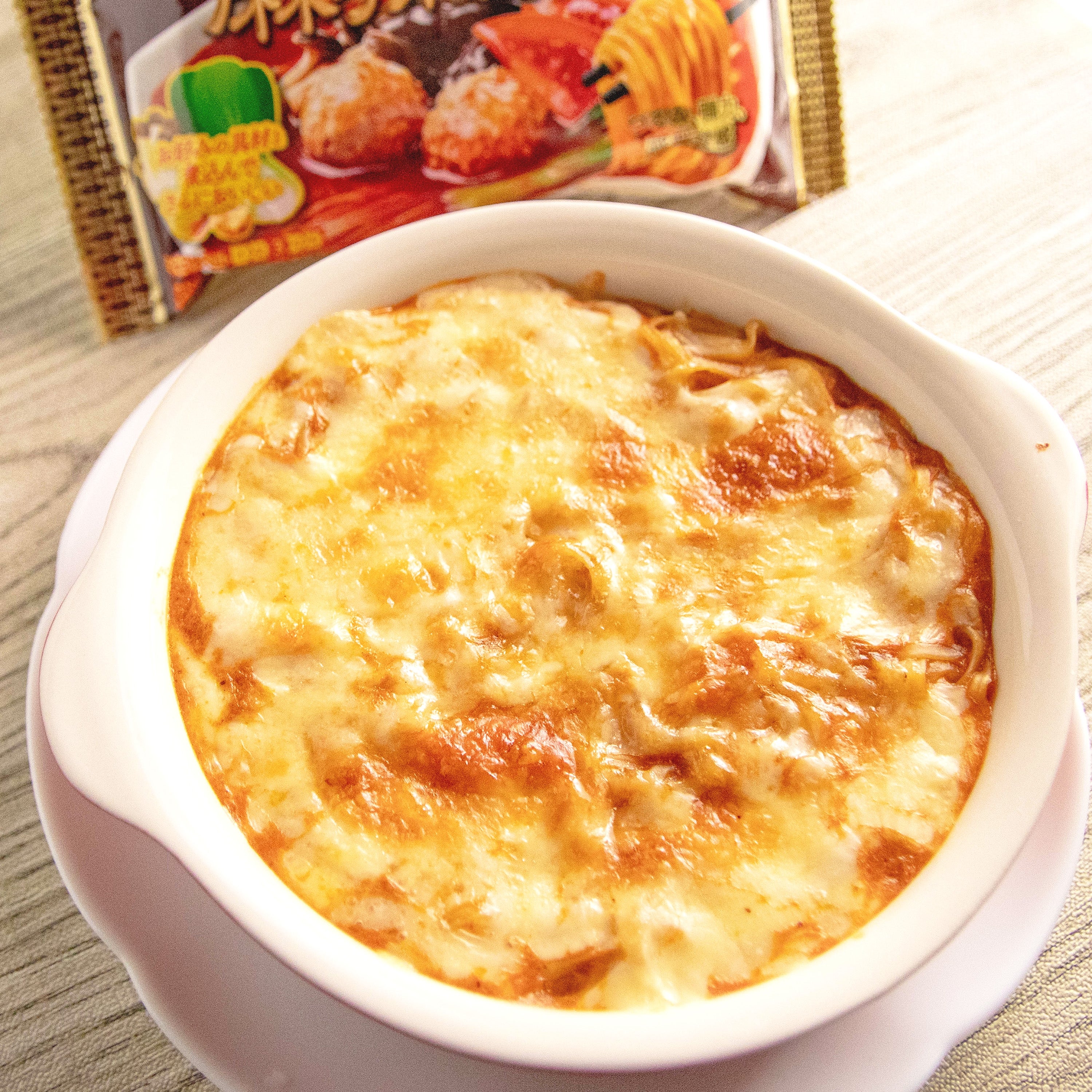 グラタンの皿がテーブルに置かれており、背景には食品パッケージが見える。