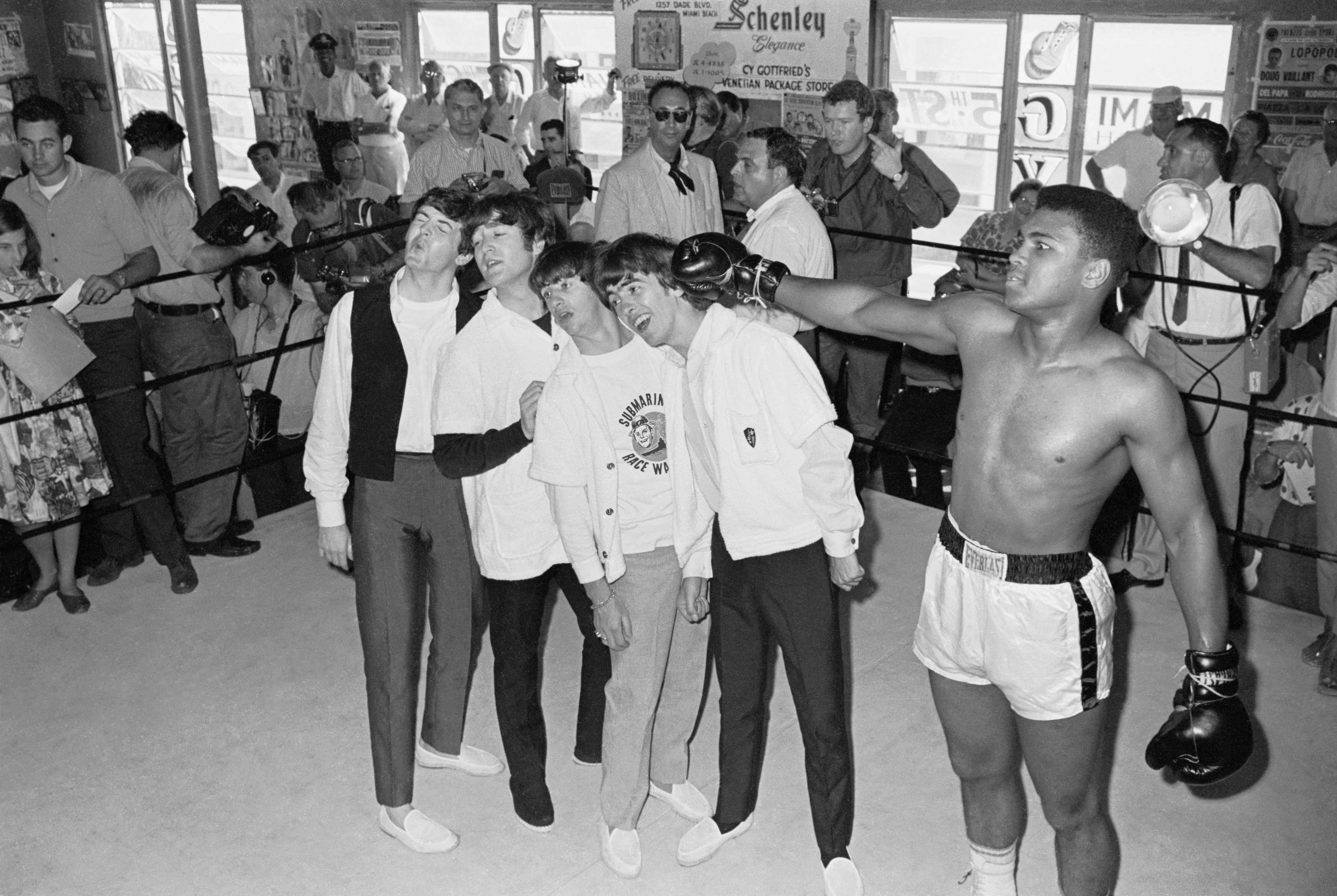 A celebrated  boxer playfully poses with 4  musicians successful  a boxing ringing  surrounded by onlookers and photographers