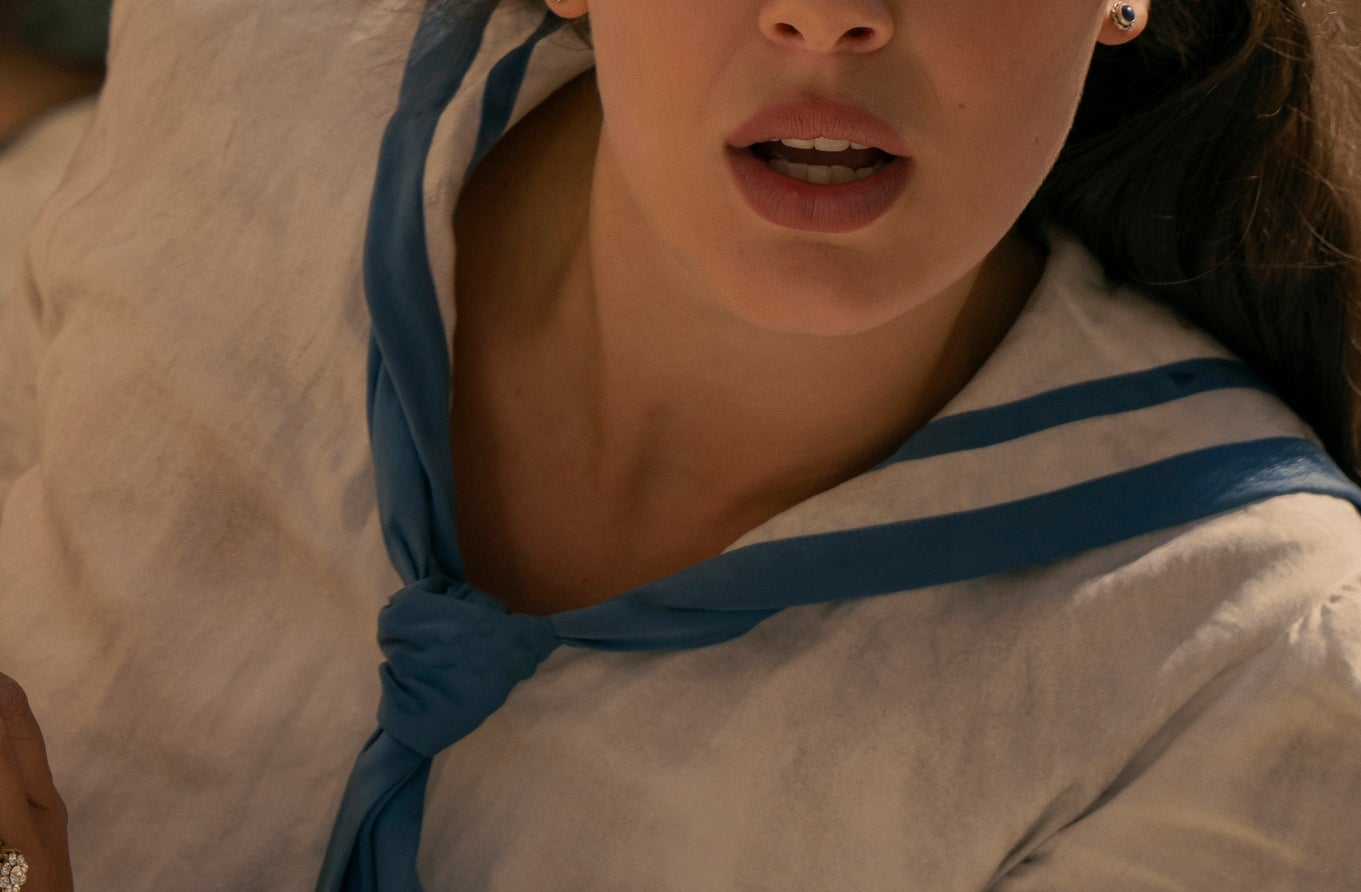 A idiosyncratic   with agelong  hair, wearing an old-fashioned achromatic  outfit with a bluish  tie, looks acrophobic   portion    peering from down  a chromatic  wall