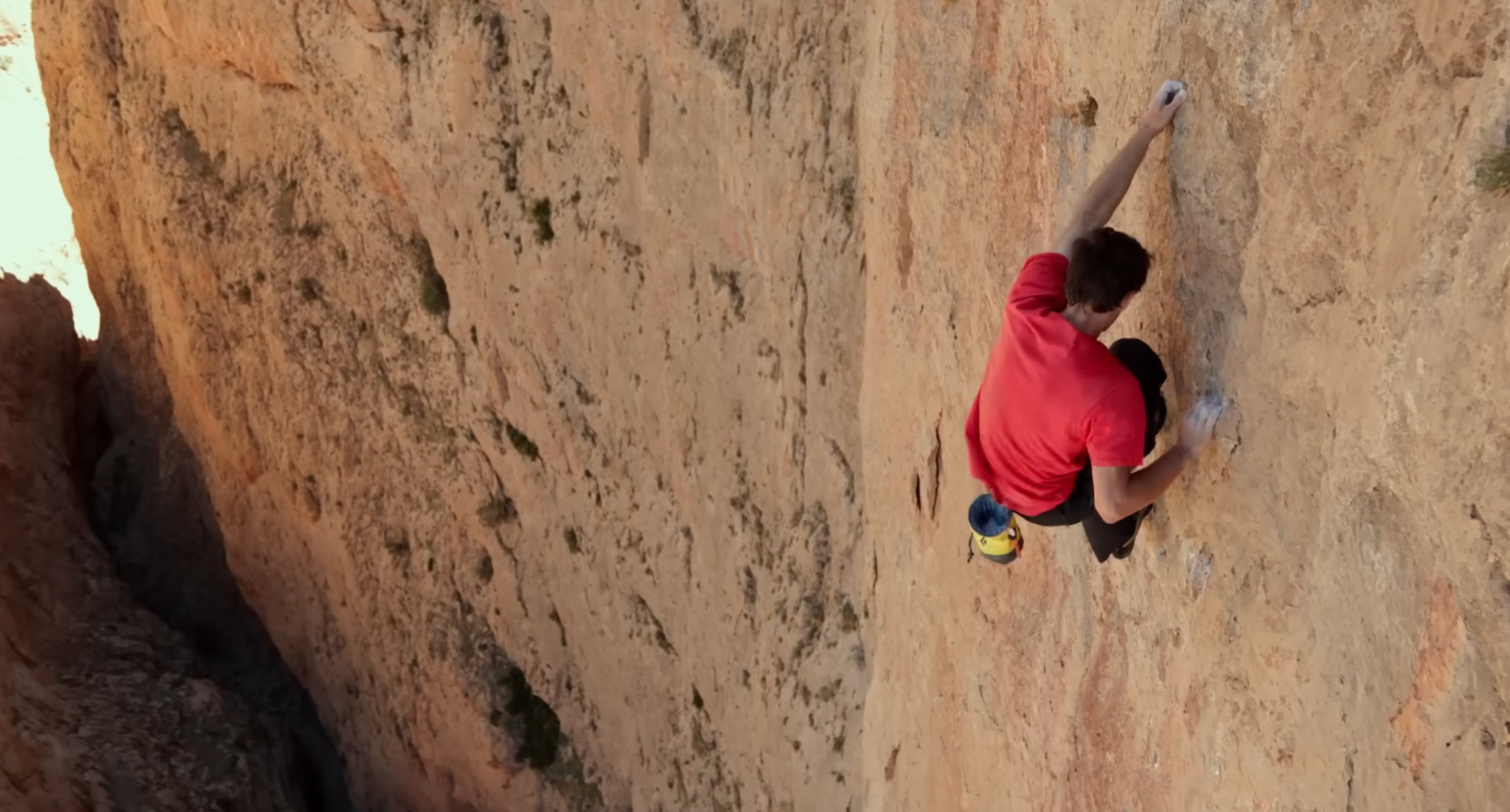 Person rock climbing a steep cliff face wearing casual attire; viewed from above
