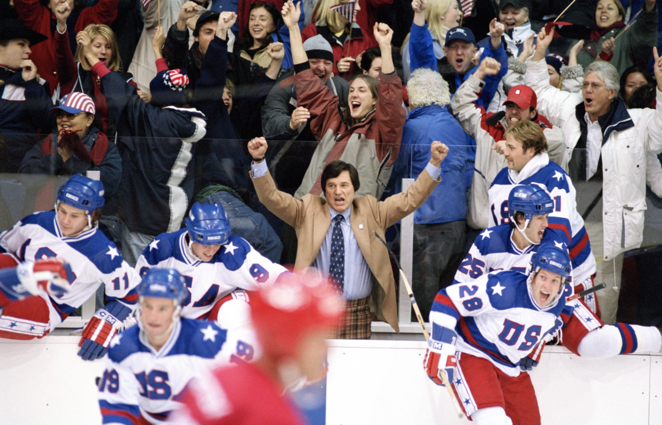 Ice hockey team celebrating a victory with cheering fans in a stadium. A coach in a suit is raising his arms in triumph