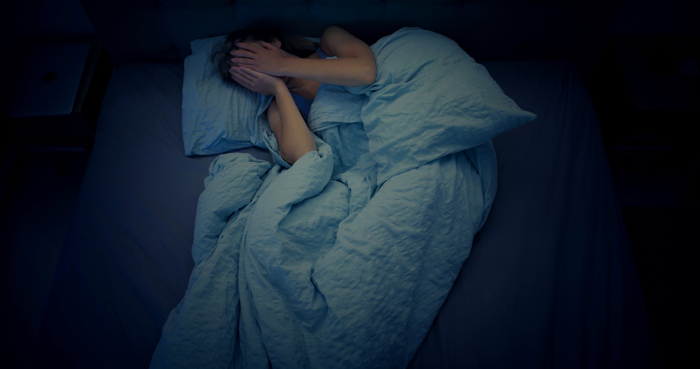 Person lying successful  furniture  nether  a broad  with hands covering their face, appearing distressed