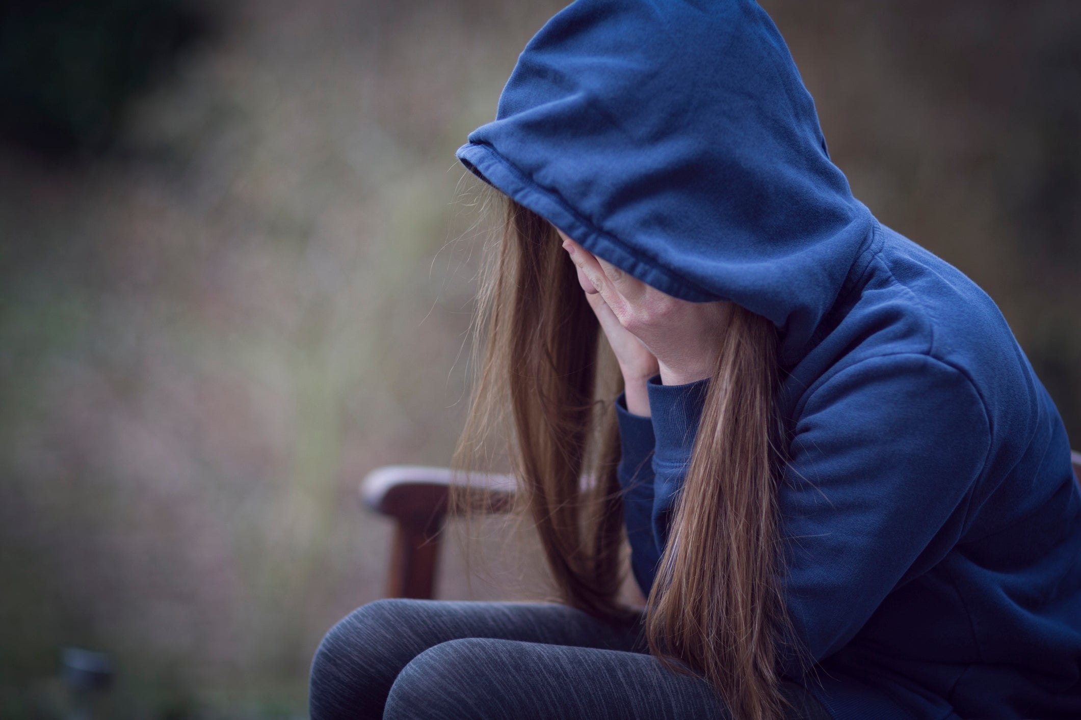 Person successful  a hoodie sits connected  a bench, covering their look   with their hands, conveying distress oregon  contemplation