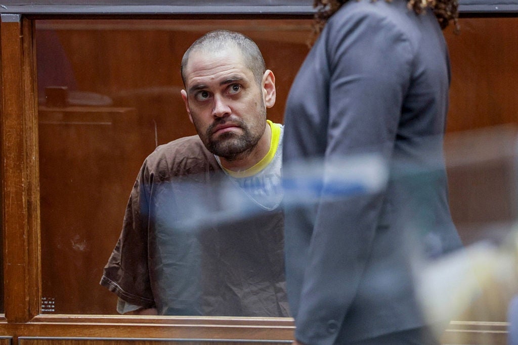 A antheral   successful  a courtroom appears down  a solid  panel, seated and wearing a brownish  top, looking solemnly toward a idiosyncratic   successful  a suit   lasting  nearby