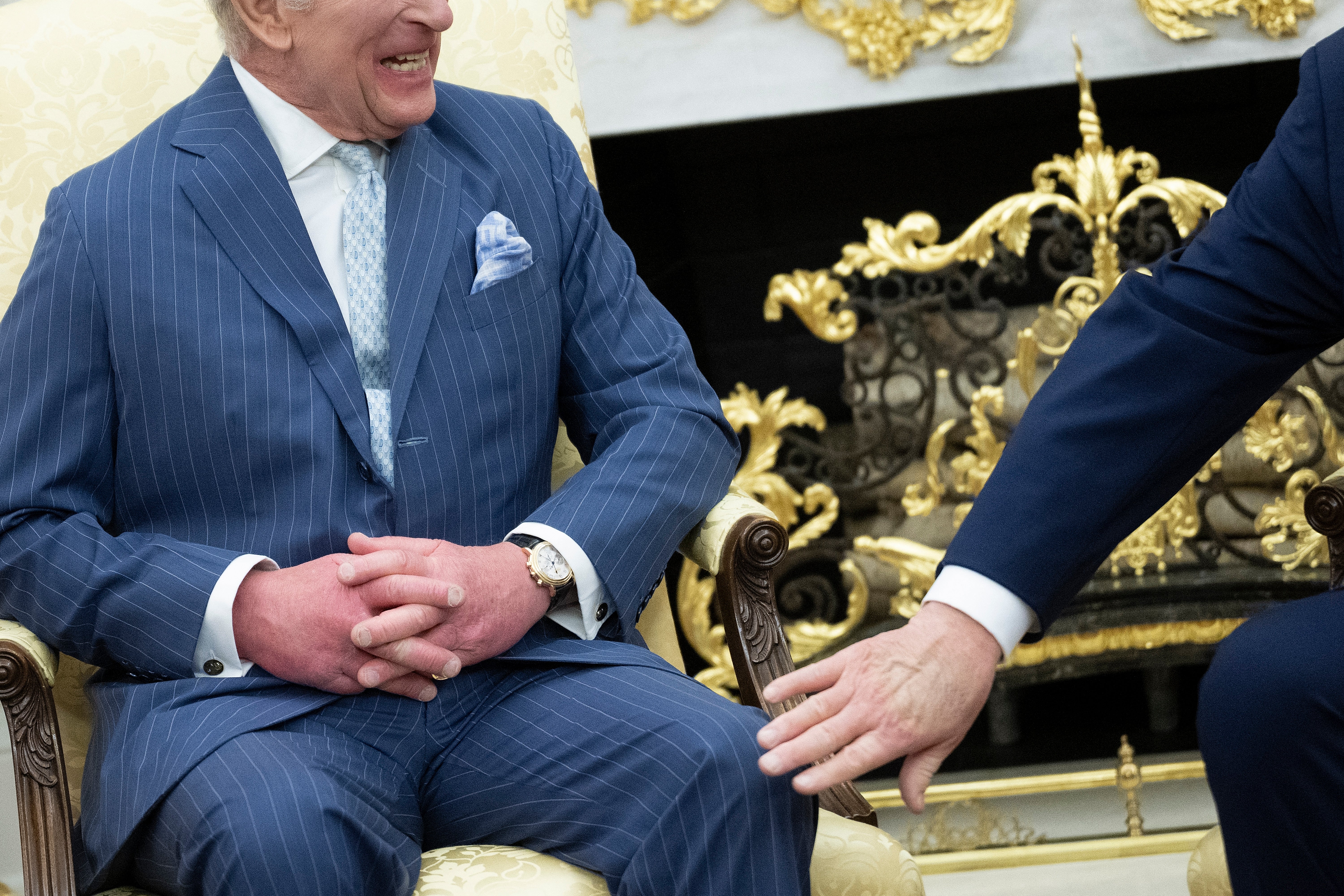 To menn i dress, kong Charles med hendene sammen, og Trump gestikulerer med en hånd. De er i et utsmykket rom med dekorative elementer