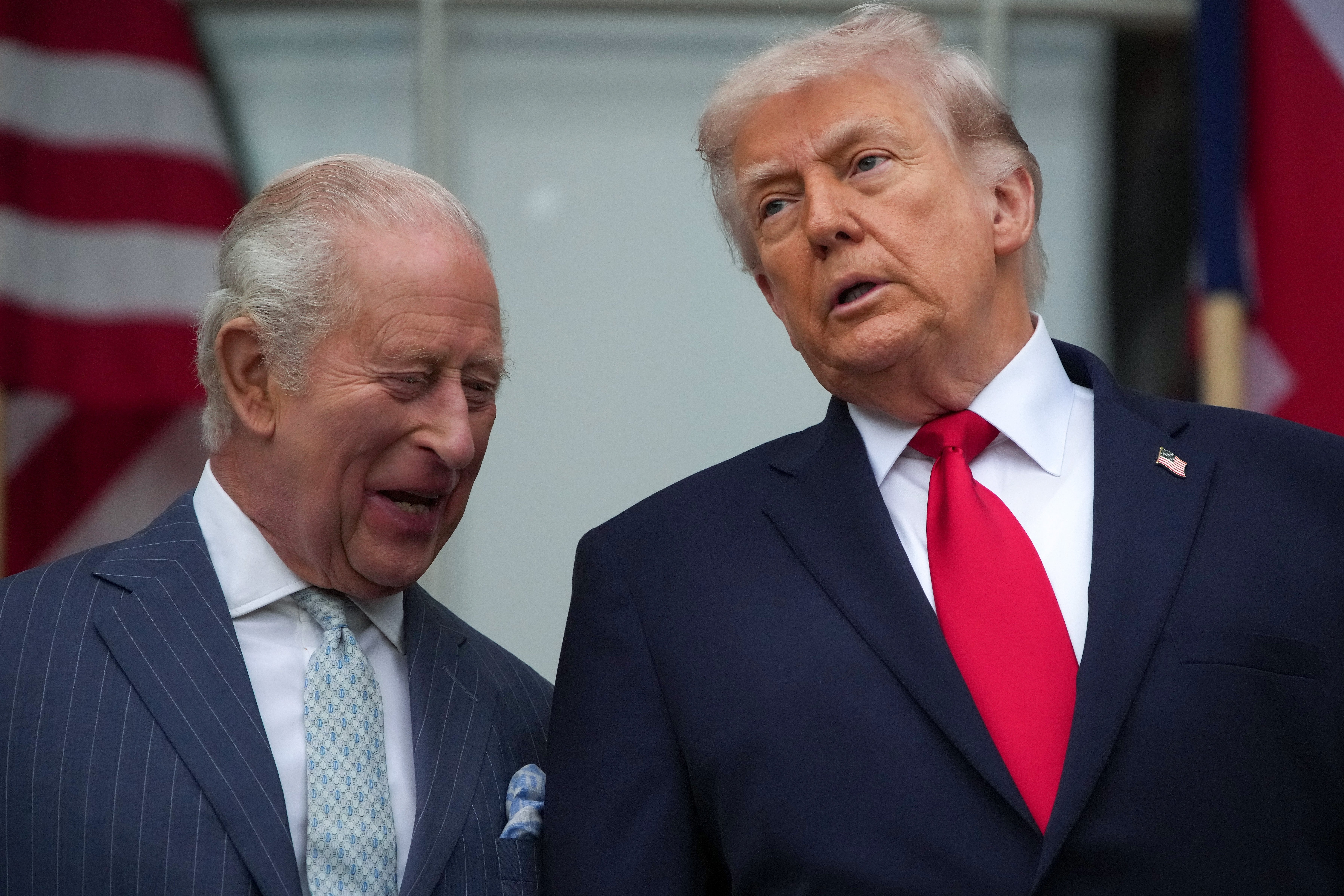 Kong Charles og Donald Trump i formelle dresser har en samtale utendørs, flagg i bakgrunnen