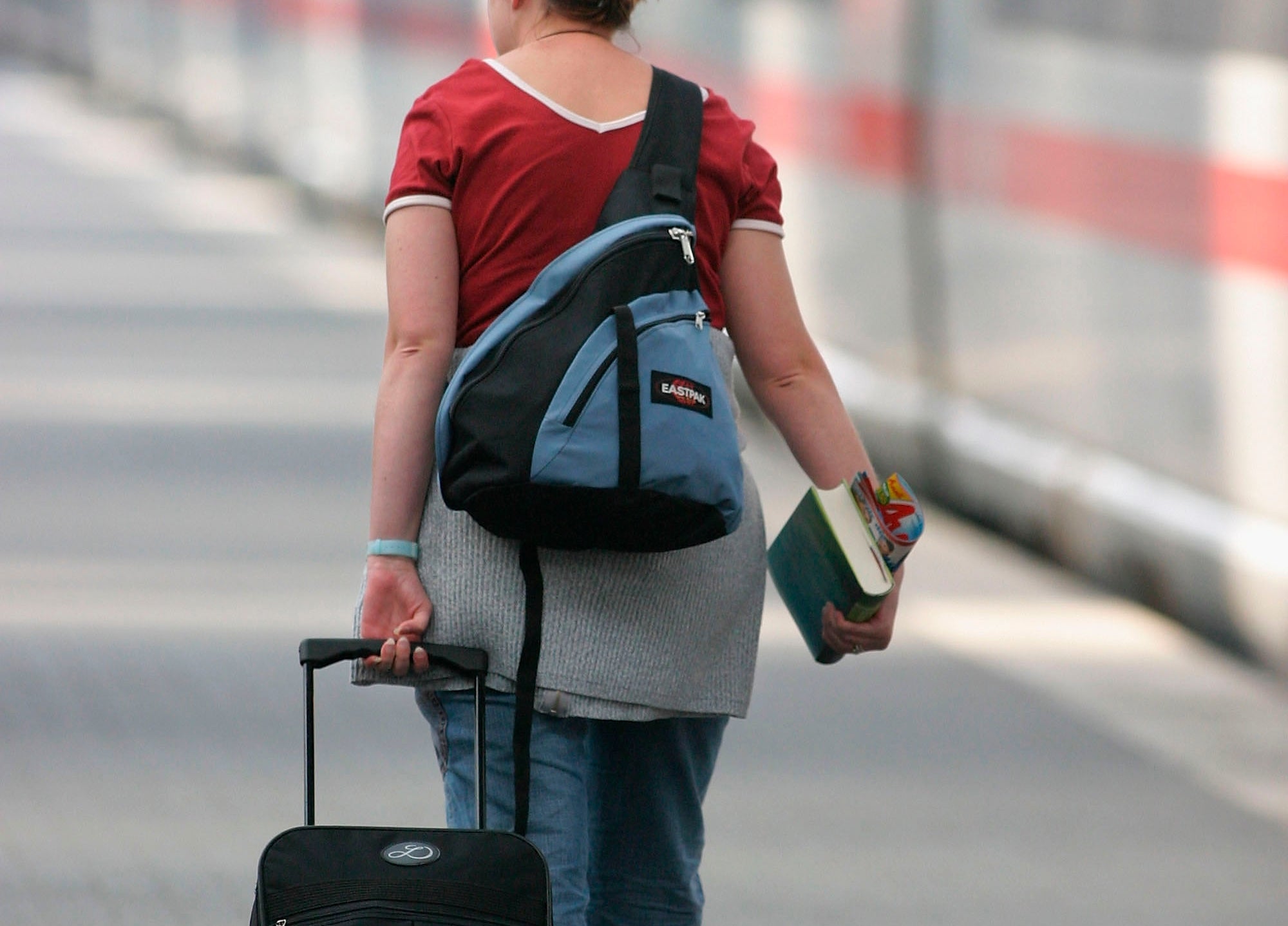 Person walking connected  a bid     level    with a suitcase and books, wearing casual attire including a reddish  apical  and jeans