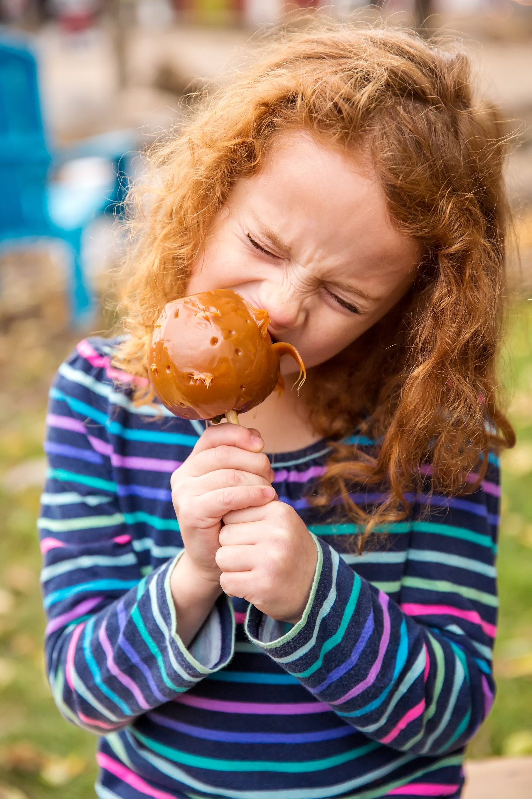 Child enjoying a caramel pome  outdoors, biting into it with eyes closed. The inheritance  is blurred, suggesting absorption   connected  the apple
