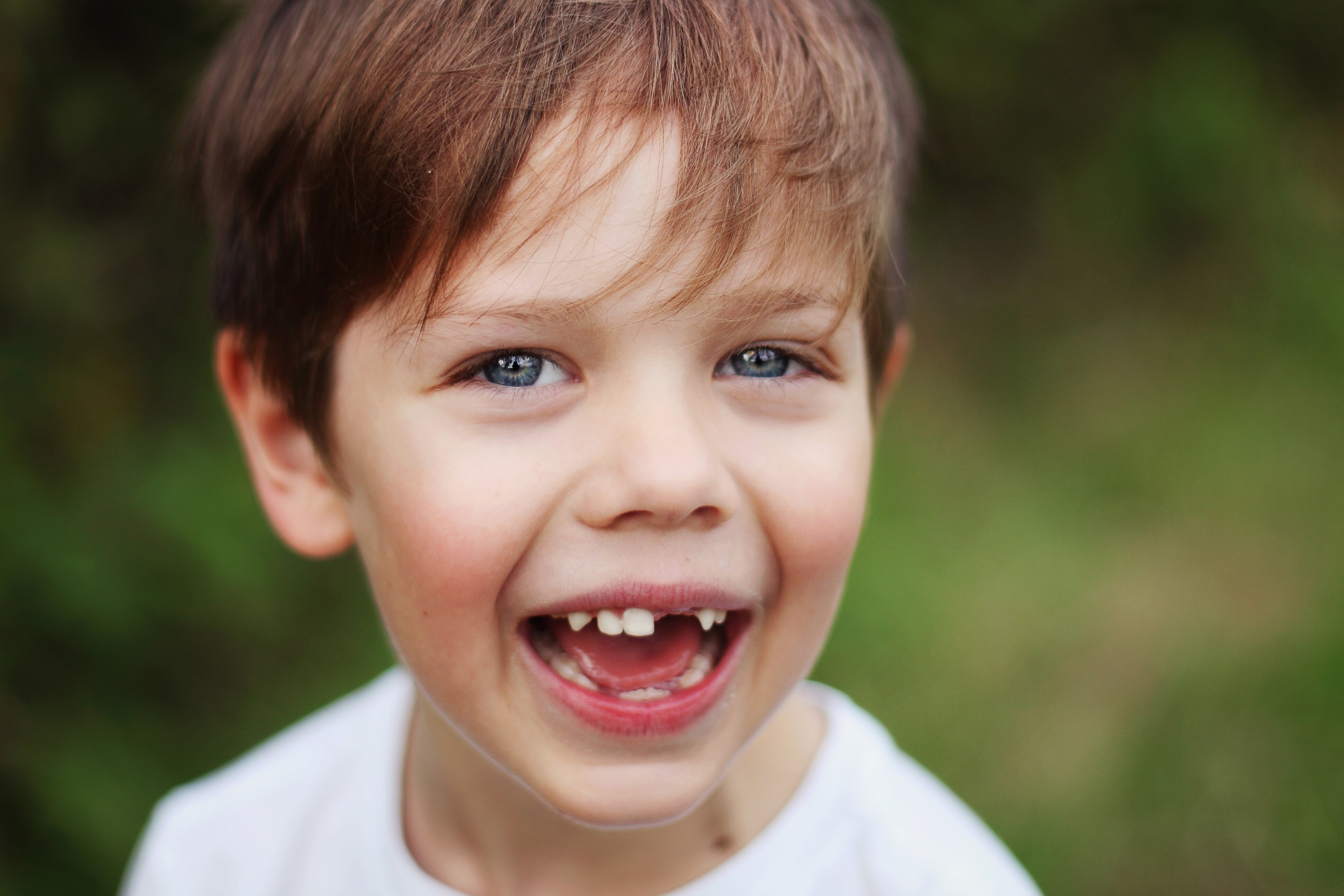 A young kid  with a joyful look  and missing beforehand   tooth, smiling outdoors