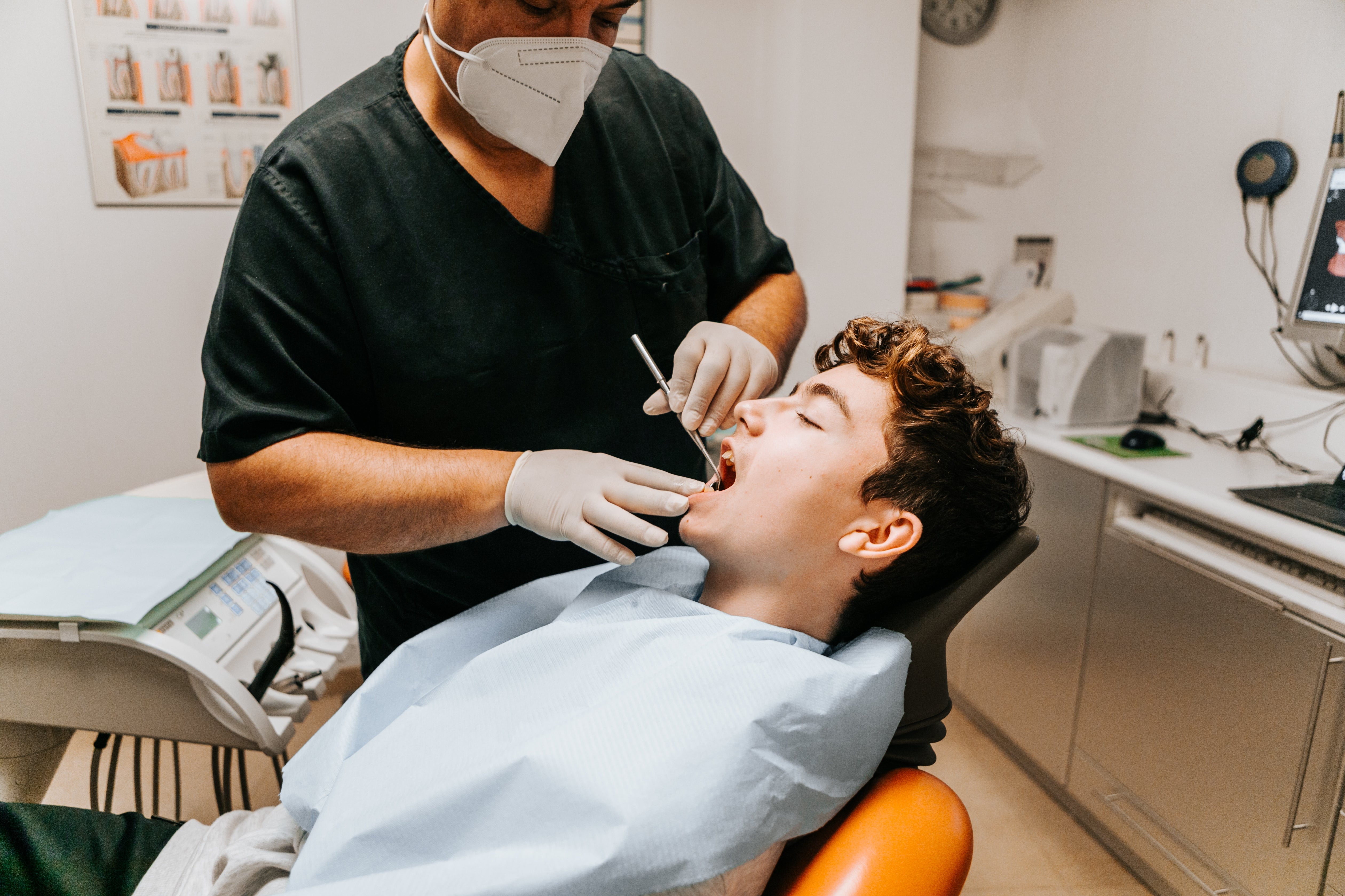 Dentist successful  scrubs examines a patient's unfastened  rima  successful  a dental chair, utilizing a dental reflector  and wearing protective gear