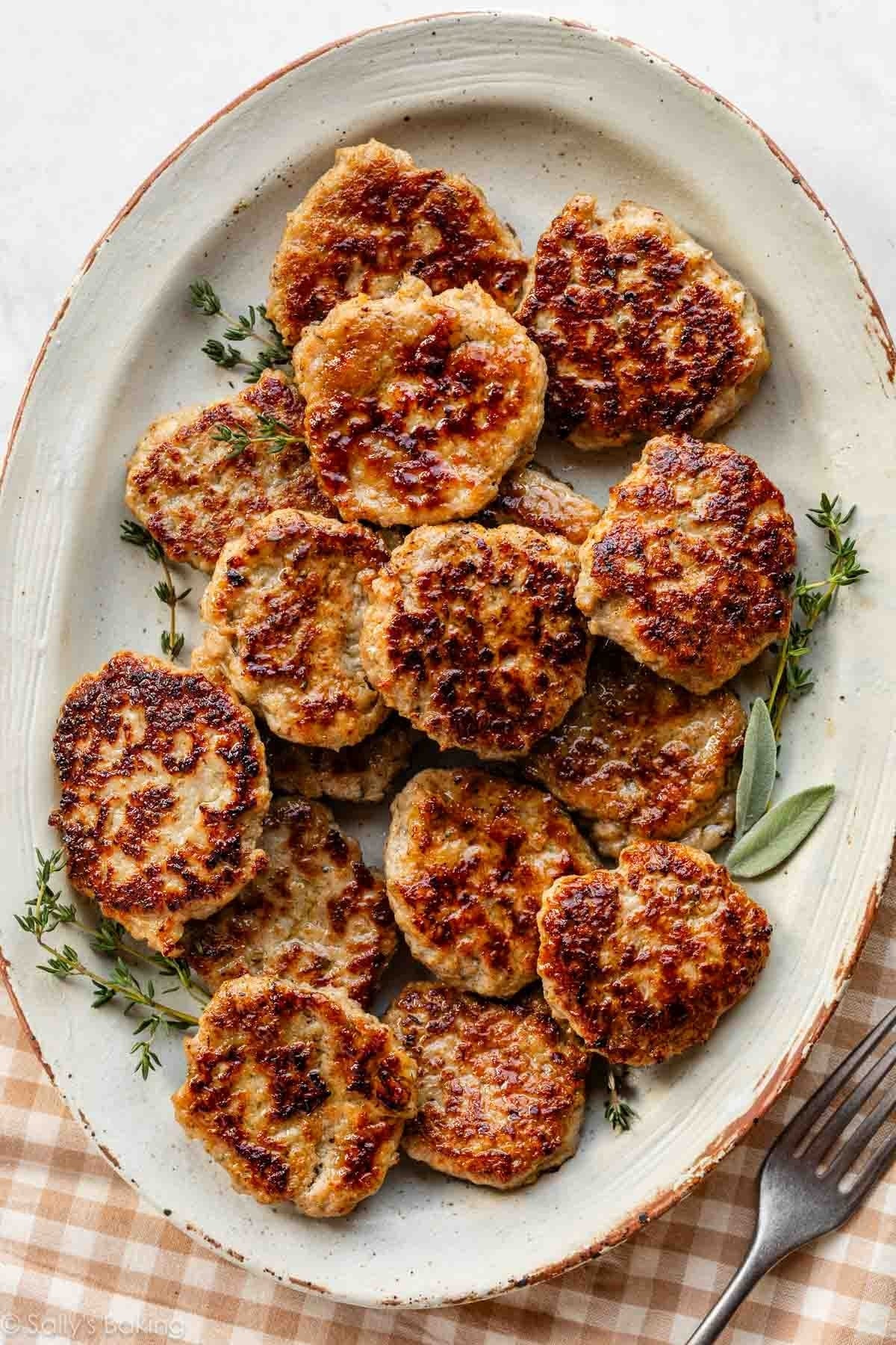 A plate of browned, cooked patties garnished with herbs on a checkered cloth, with a fork on the side