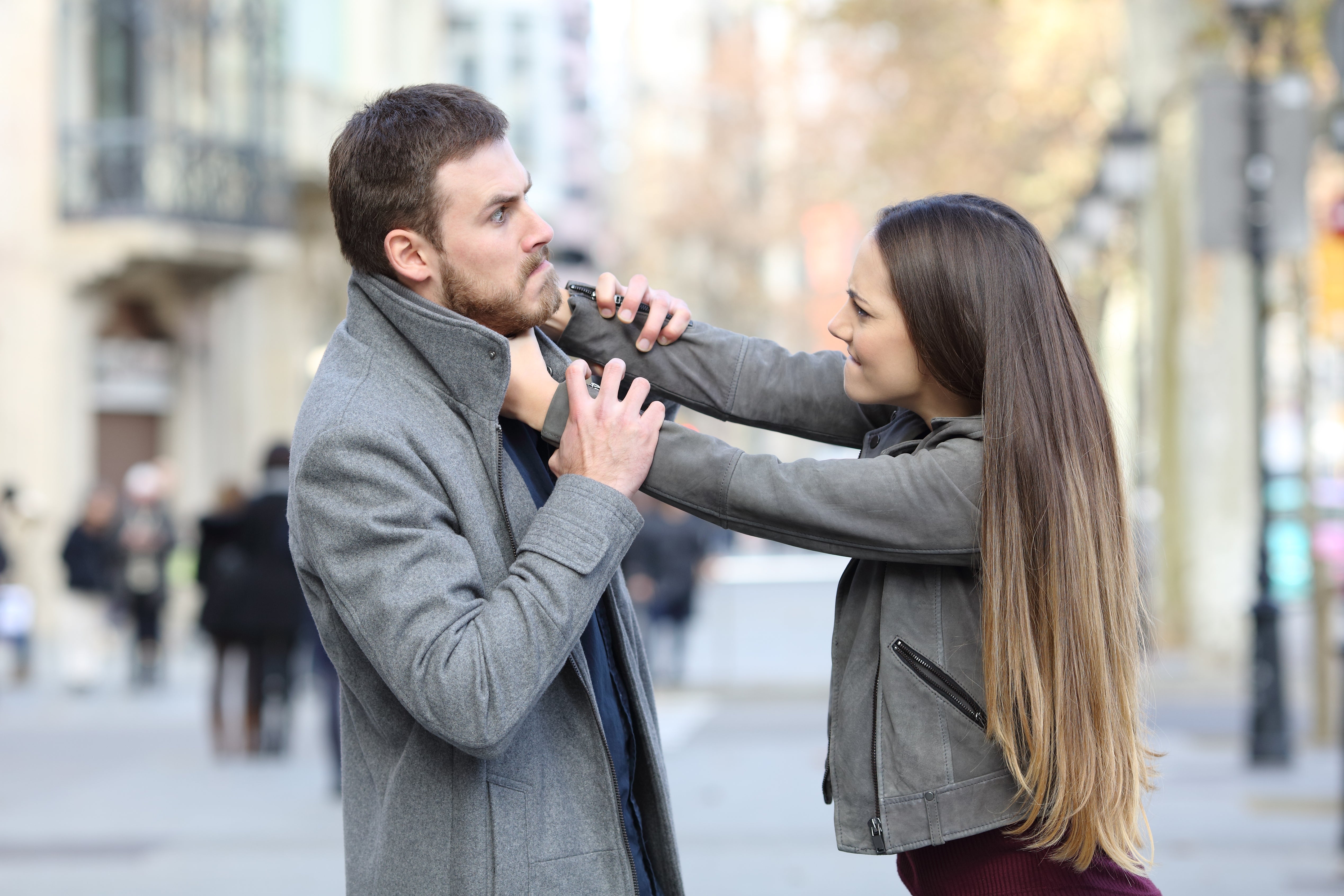 Woman playfully straightening a man's overgarment  collar connected  a street, some  smiling