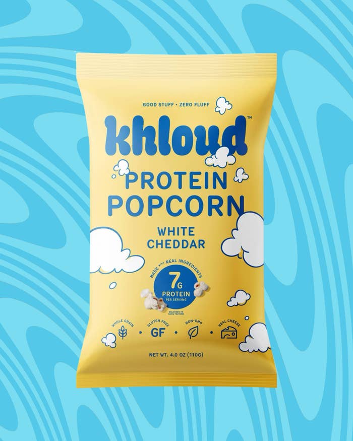 Bag of "Khloud Protein Popcorn, White Cheddar" on a blue swirling background, highlighting 7g protein, gluten-free, made with real ingredients