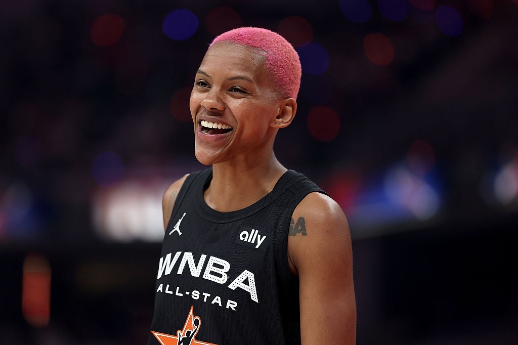 Person i en ermeløs WNBA-trøye smiler bredt ved et arrangement