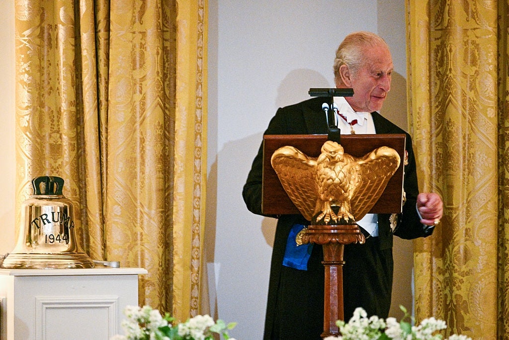 An aged  antheral   successful  a tuxedo stands astatine  a podium with a aureate  eagle design, adjacent  to a doorbell  labeled "1944," amidst lavish curtains