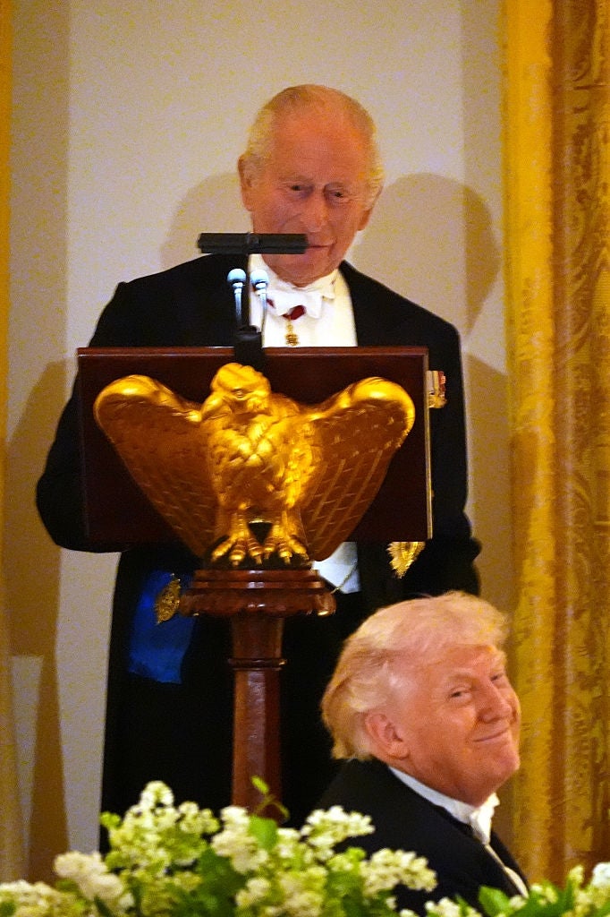 A idiosyncratic   successful  ceremonial  attire stands astatine  a podium with an eagle design, portion    different  idiosyncratic   smiles seated adjacent  to it