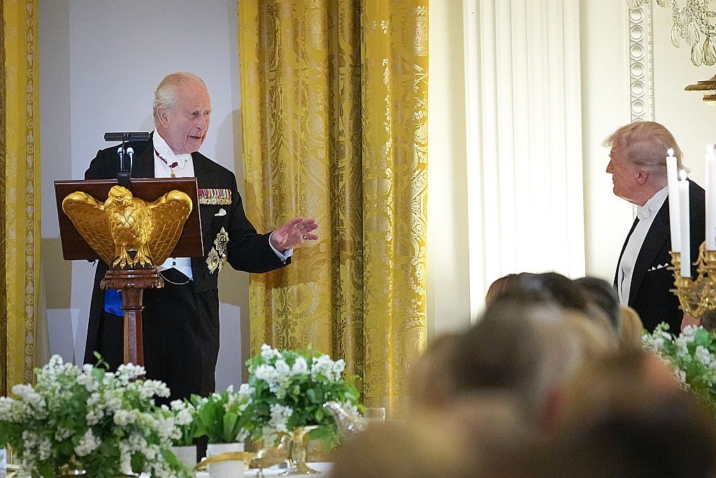 Two men successful  ceremonial  attire astatine  a podium during an elegant meal  event. One is speaking, the different   listening. The mounting  is luxurious with ornate decor