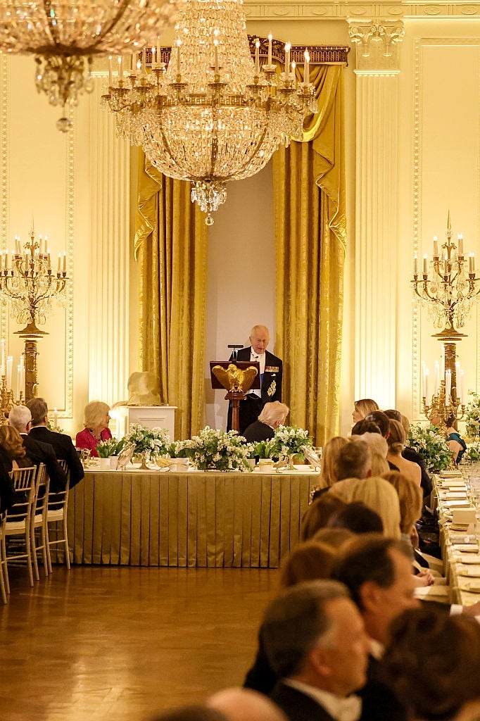 A ceremonial  banquet country   with a talker  astatine  a podium successful  an ornate hall, surrounded by elegantly dressed guests seated astatine  agelong  tables