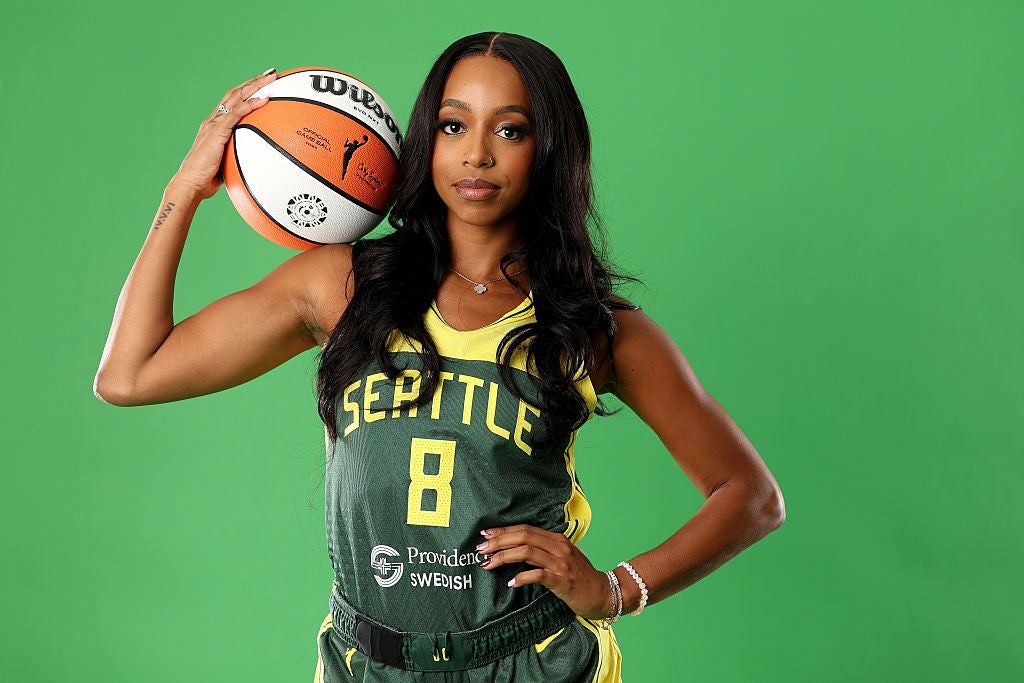 En basketballspiller i en Seattle-trøye med "8" står og holder en ball på skulderen mot et grønt bakteppe