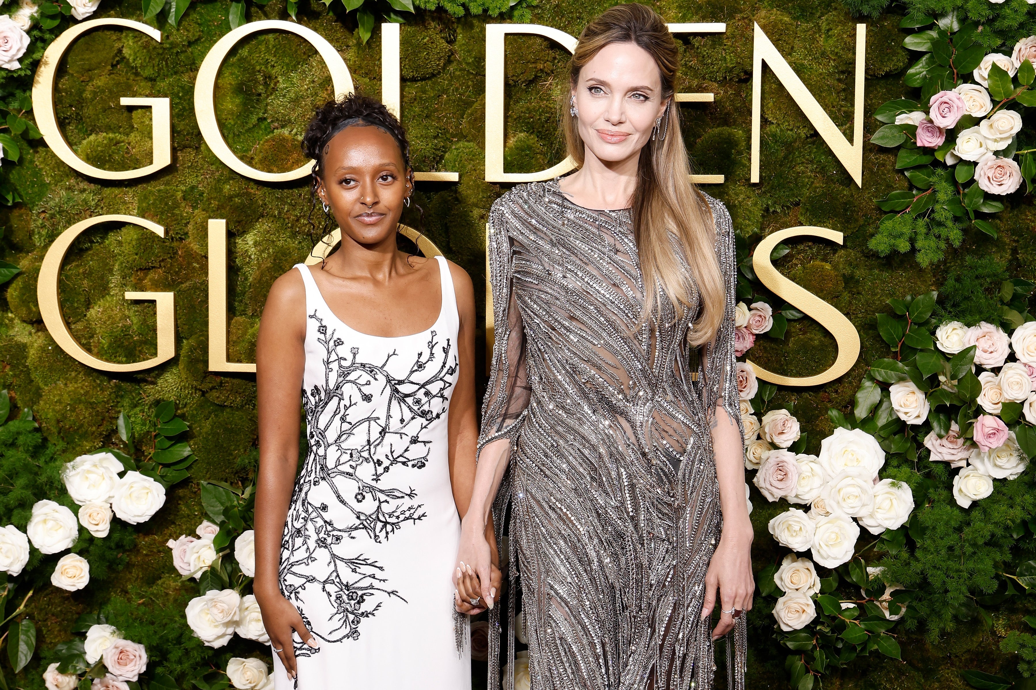 Two women connected  a reddish  carpet, 1  successful  a achromatic  floral gown and the different   successful  a shimmering metallic  dress, airs  elegantly successful  beforehand   of a floral backdrop