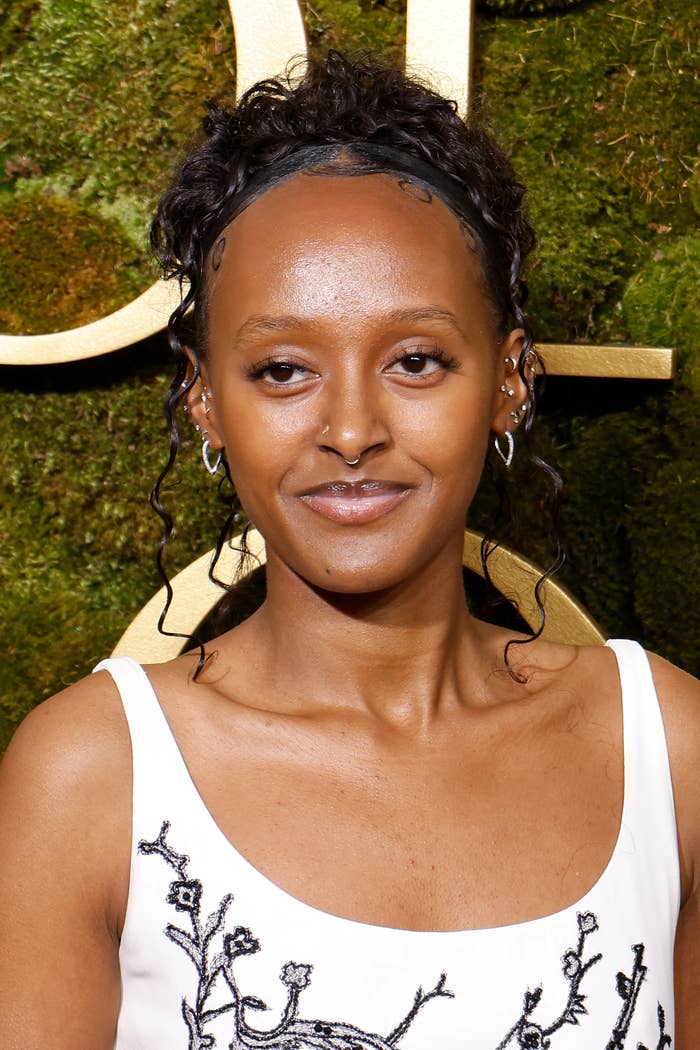 Person wearing a achromatic  formal  with achromatic  floral embroidery astatine  an event, posing successful  beforehand   of a greenish  and golden  backdrop