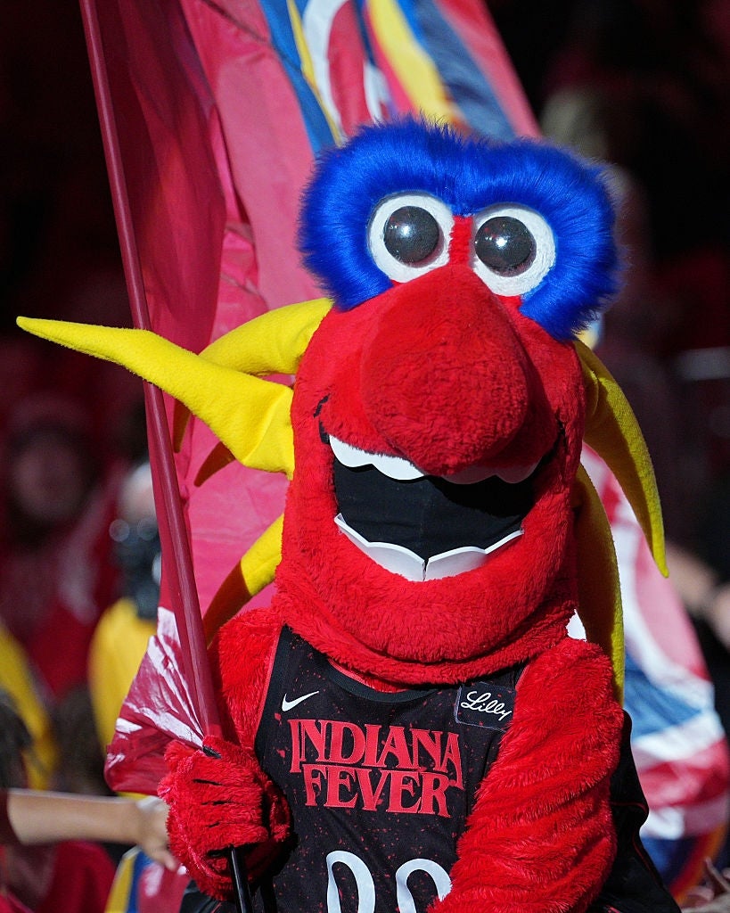 A reddish  and yellowish  mascot with a ample  feathered caput  holds a emblem  astatine  a sports event, wearing an Indiana Fever jersey