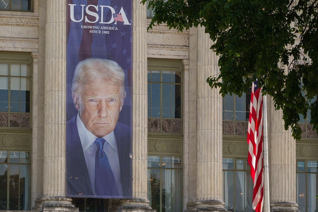 Et stort banner av en person vises på en USDA-bygning, med deres seriøse uttrykk. Et amerikansk flagg er synlig ved siden av