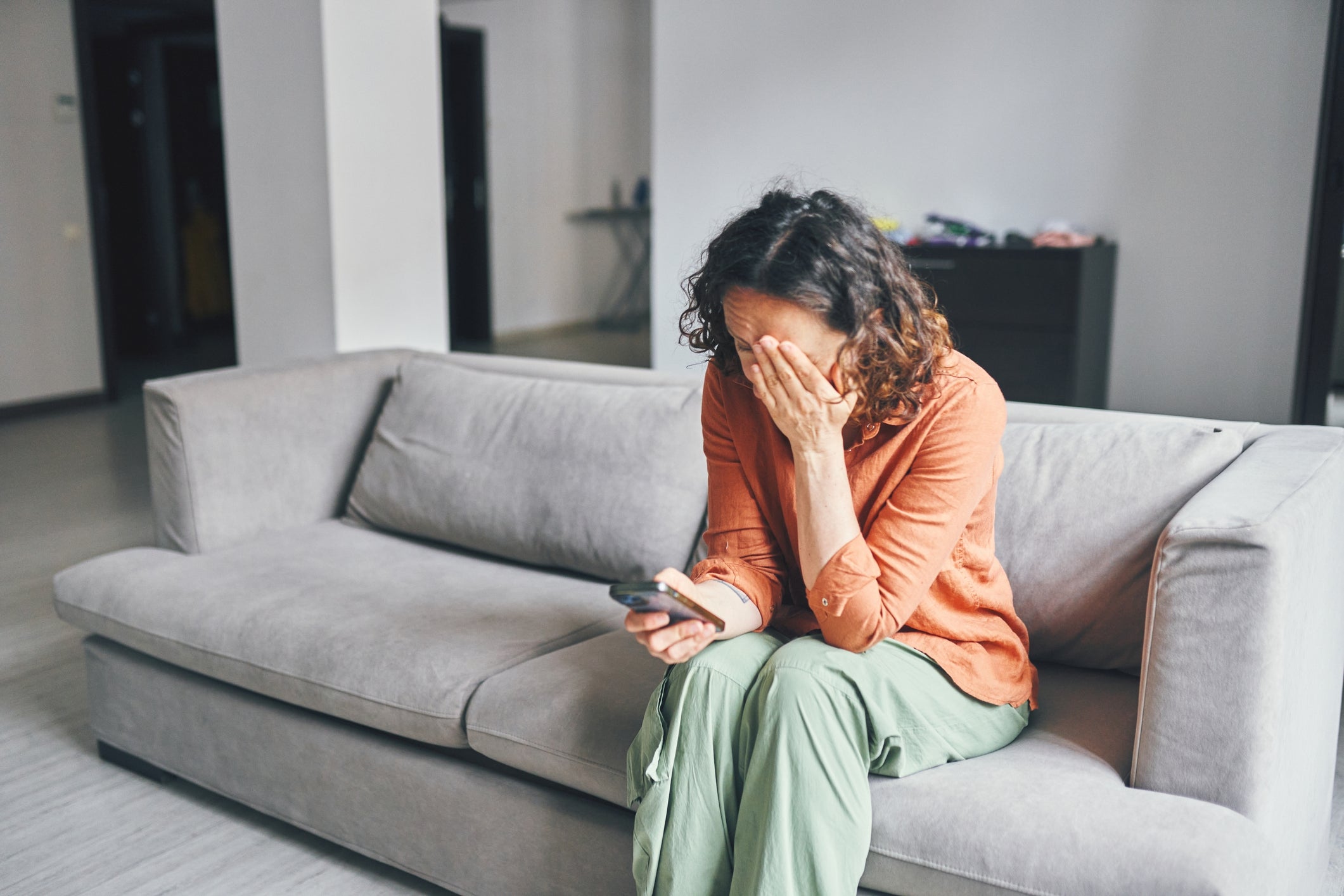 A idiosyncratic   sitting connected  a couch, holding a telephone  and covering their look   with 1  hand, appearing distressed oregon  upset