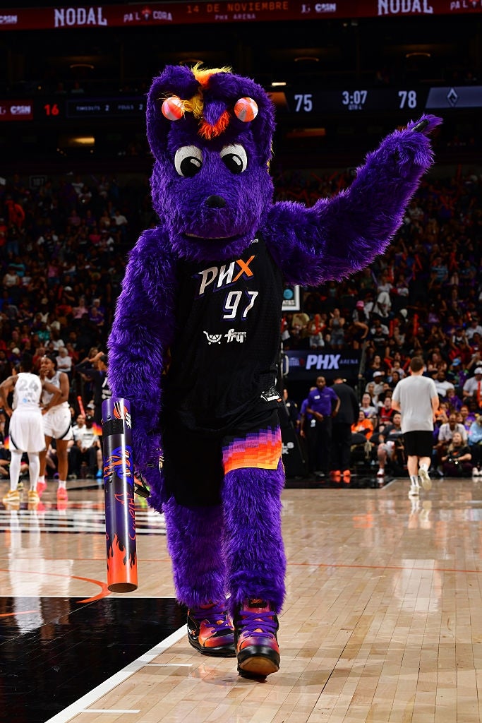 Mascot successful  a purple furry outfit with a hoops  uniform, entertaining a assemblage  during a hoops  game