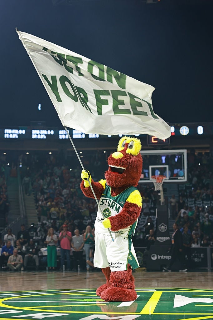 Basketball mascot connected  tribunal  waving a ample  emblem  that reads "GET ON YOUR FEET," engaging the assemblage  during a game