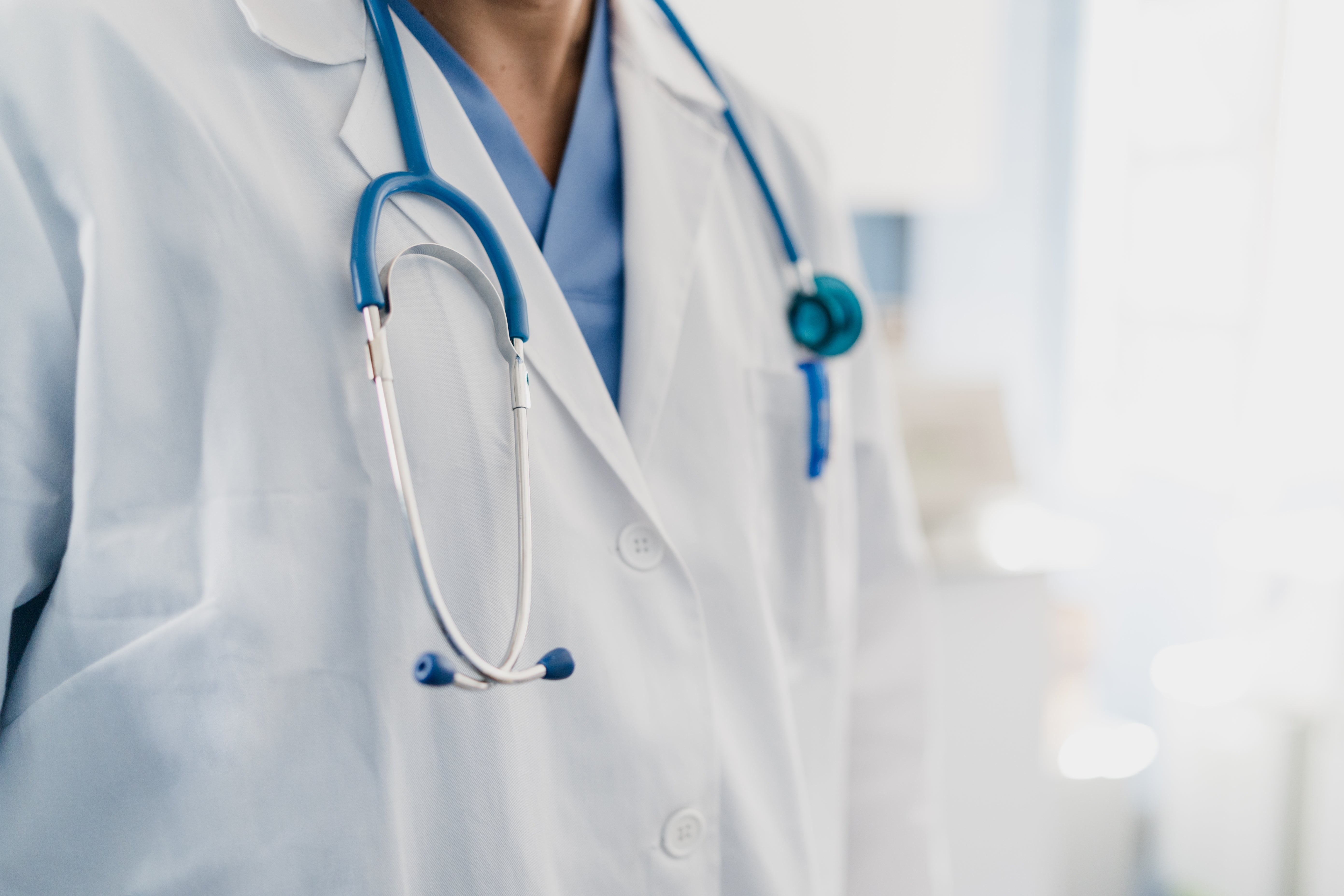 Doctor with a stethoscope wearing a achromatic  overgarment  and bluish  scrubs, lasting  successful  a objective  setting