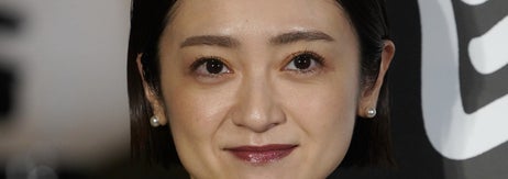 女性がチェック柄の着物と花柄の帯を身に着け、微笑んでいる。背景には漢字が見える。