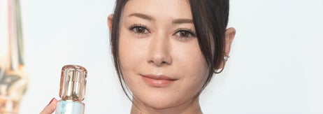 女性がレースのドレスで美容製品のボトルを持っている。