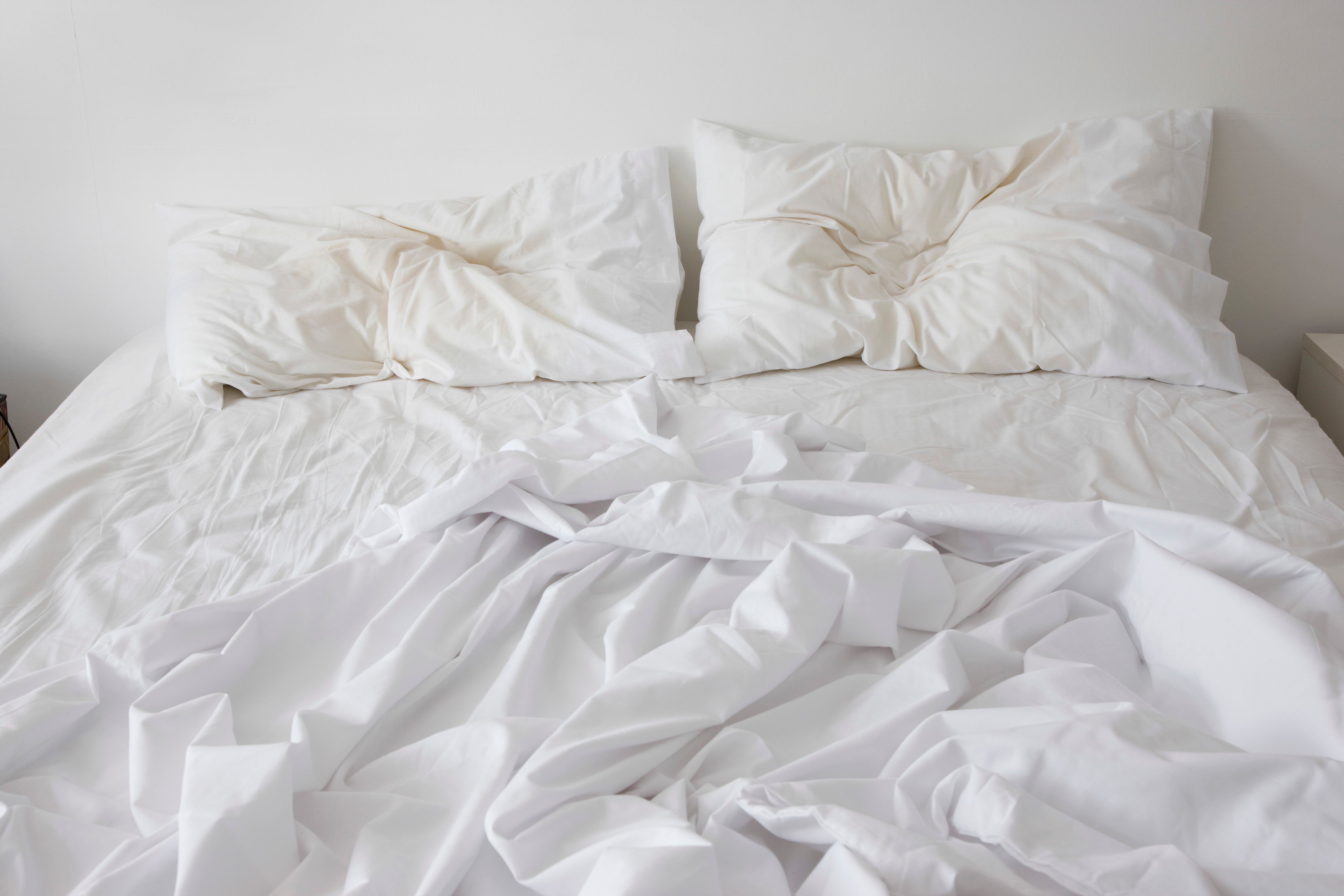 Unmade bed with white sheets and pillows, conveying an everyday relaxed atmosphere