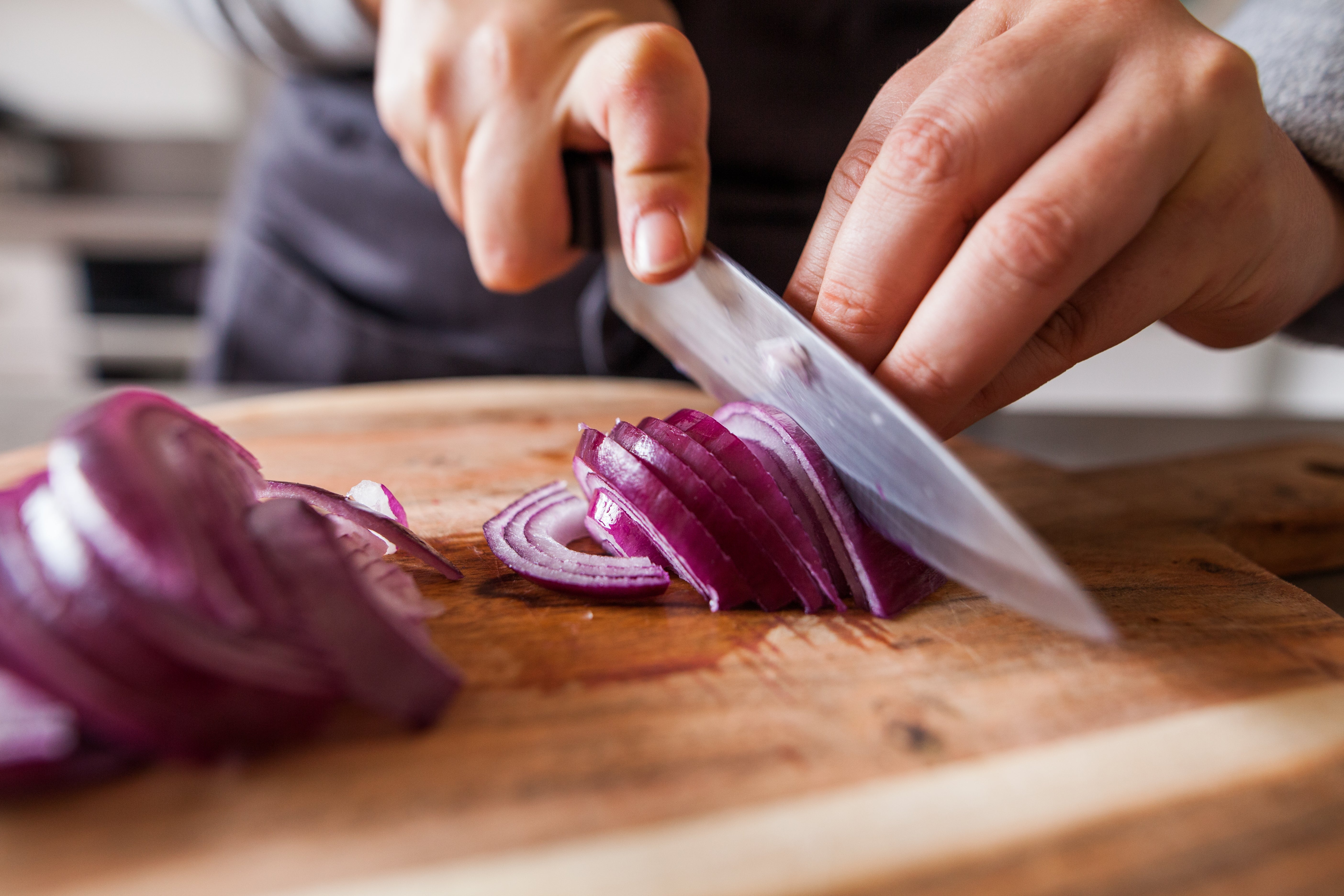 Person slicing an onion with a large knife on a wooden cutting board, highlighting cooking skills or meal preparation