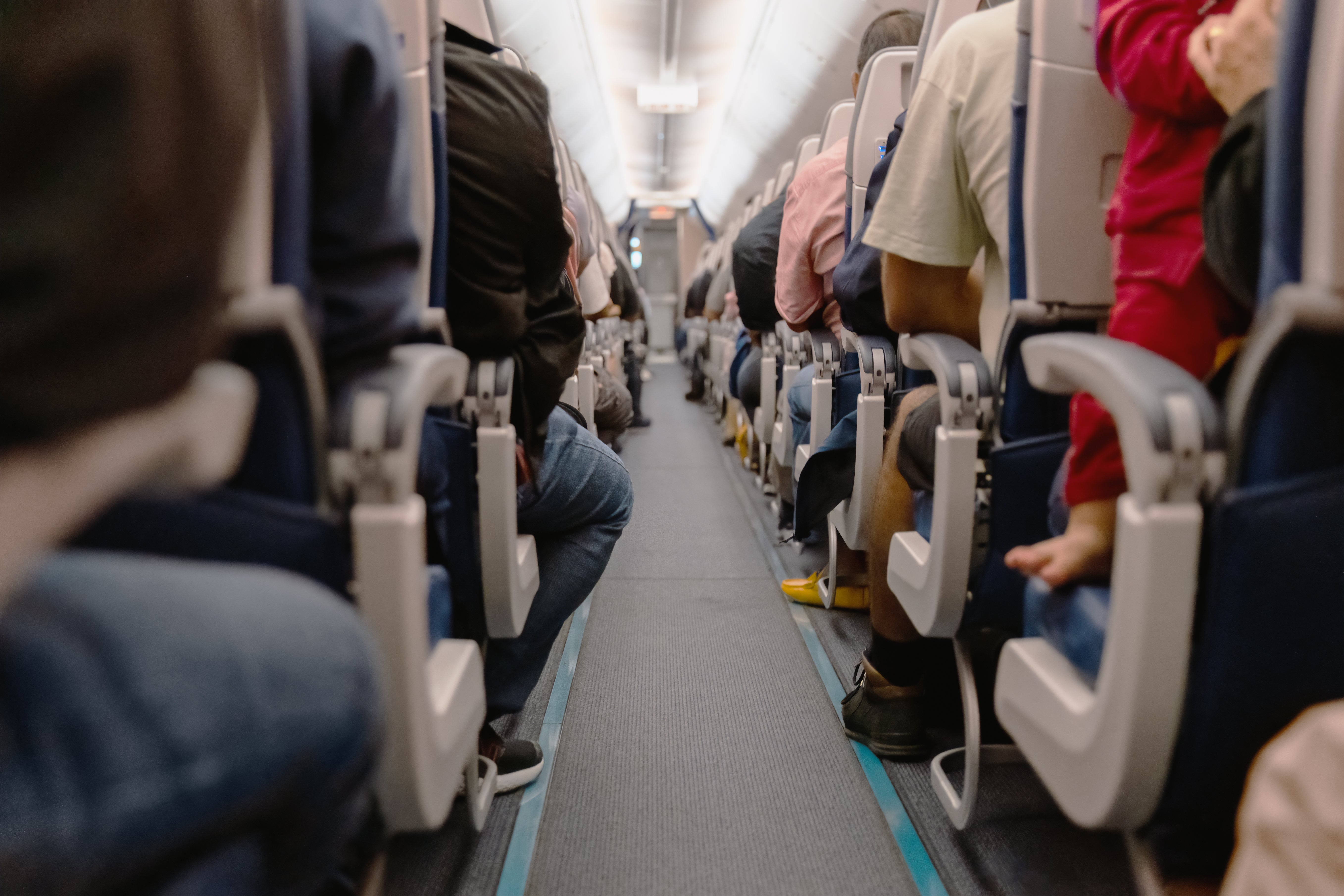 Passengers seated in an airplane cabin, viewed from the aisle, suggesting travel or commuting