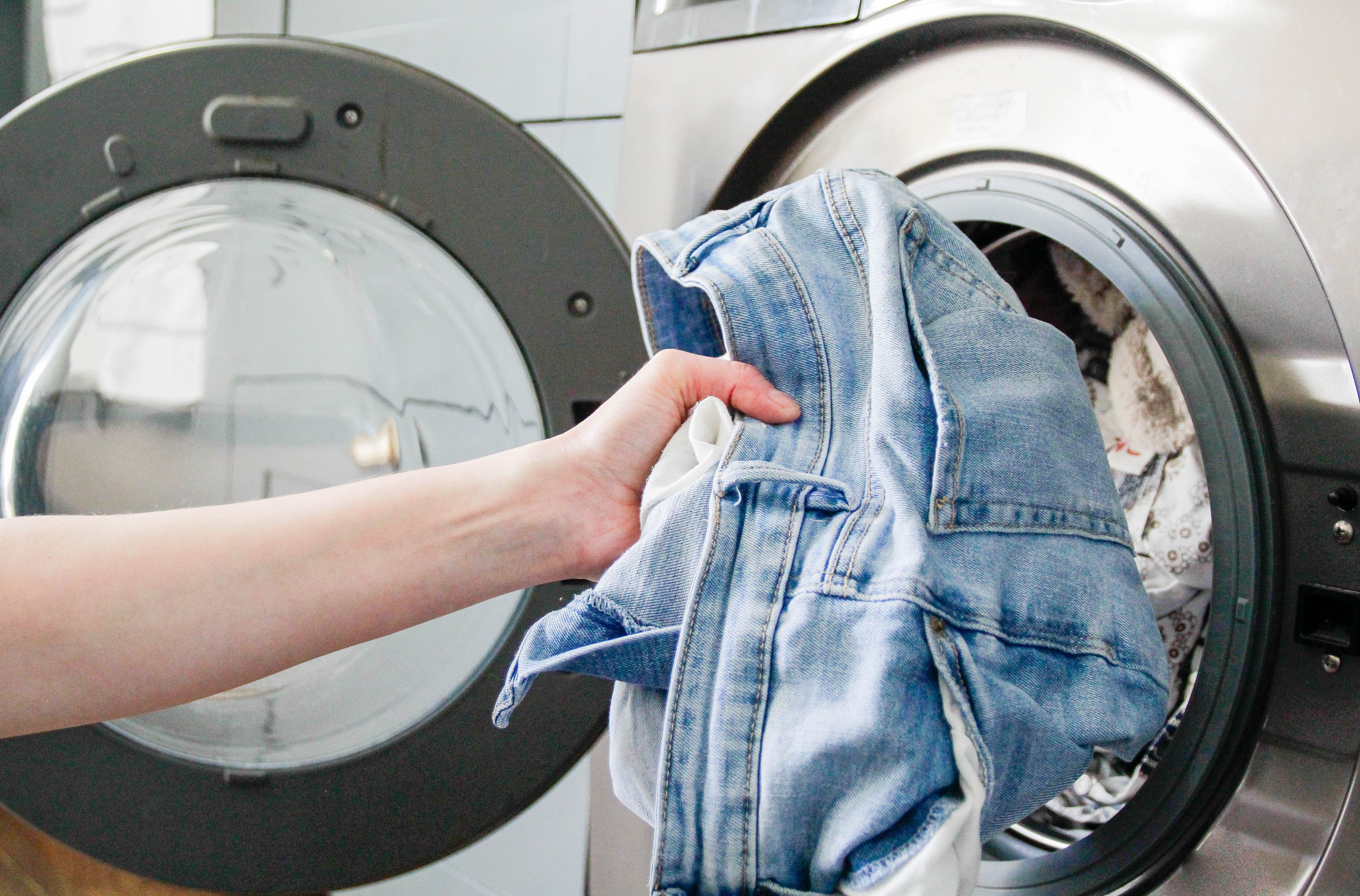Person loading denim jacket into a front-loading washing machine, symbolizing domestic chores and personal finance management