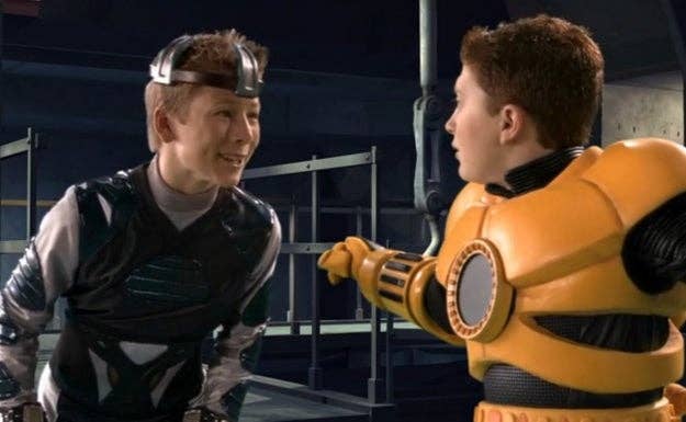 Two kids successful  futuristic costumes, 1  successful  a metallic outfit, the different   successful  orangish  armor, successful  a sci-fi setting, engaged successful  conversation
