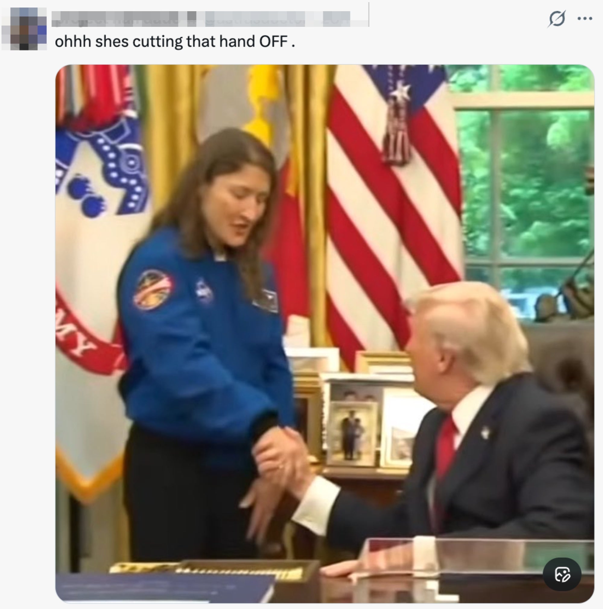 En person i en NASA-uniform håndhilser på en mann i dress i et offisielt utseende; flagg er synlige i bakgrunnen