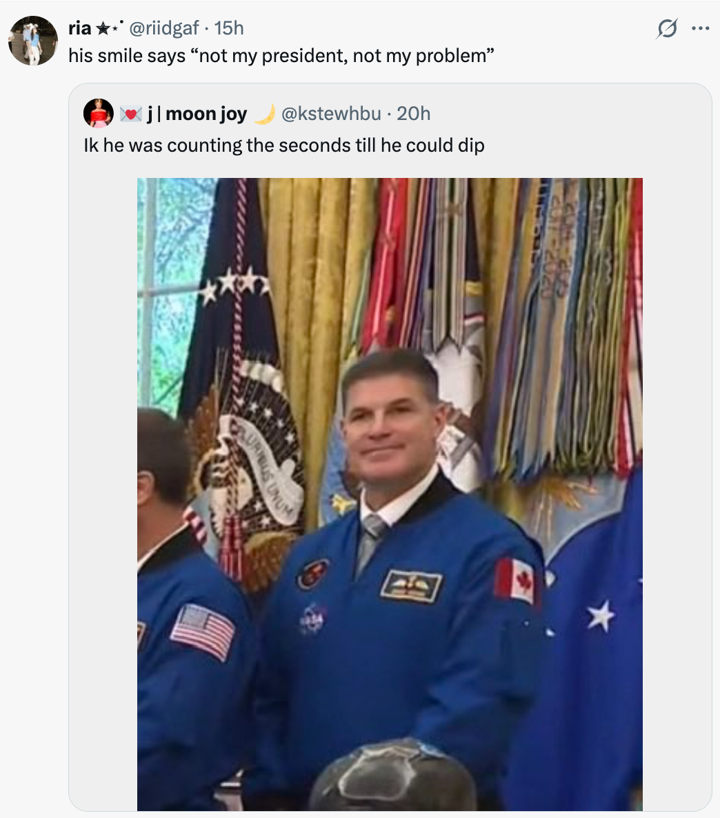 Astronaut i blå jumpsuit står i et dekorert rom med forskjellige flagg og presidentsegl synlig