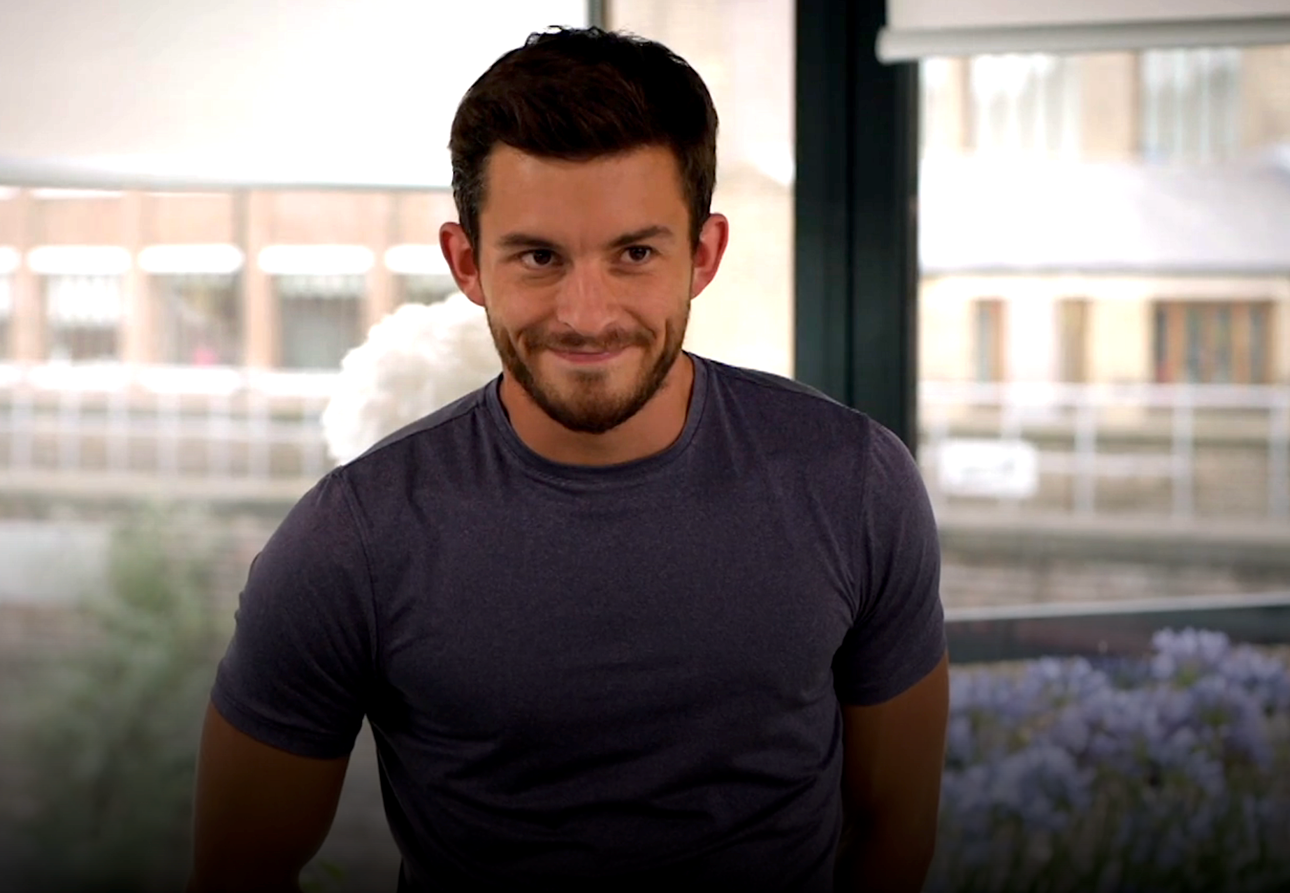 Person smiling, wearing a short-sleeve shirt, lasting  indoors adjacent   a window