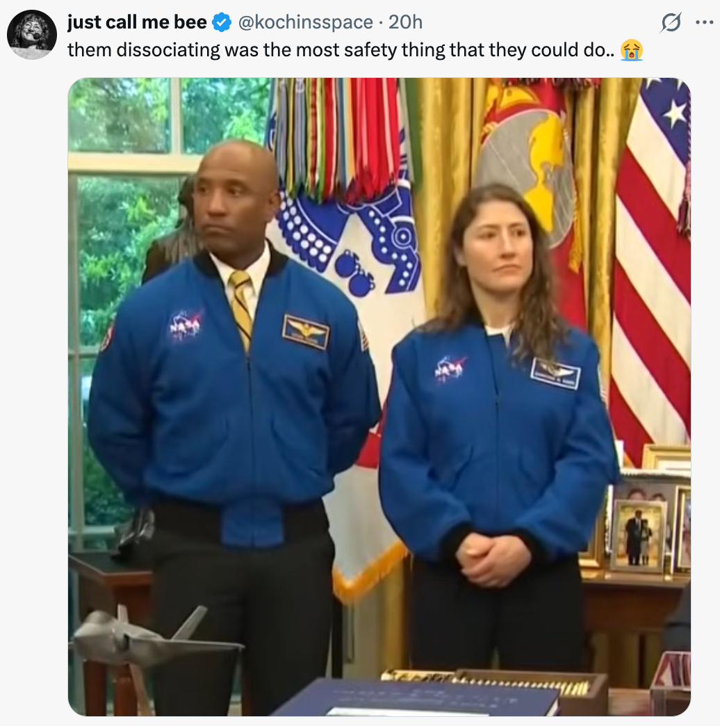 To NASA-astronauter står innendørs i blå flydrakt under en formell begivenhet