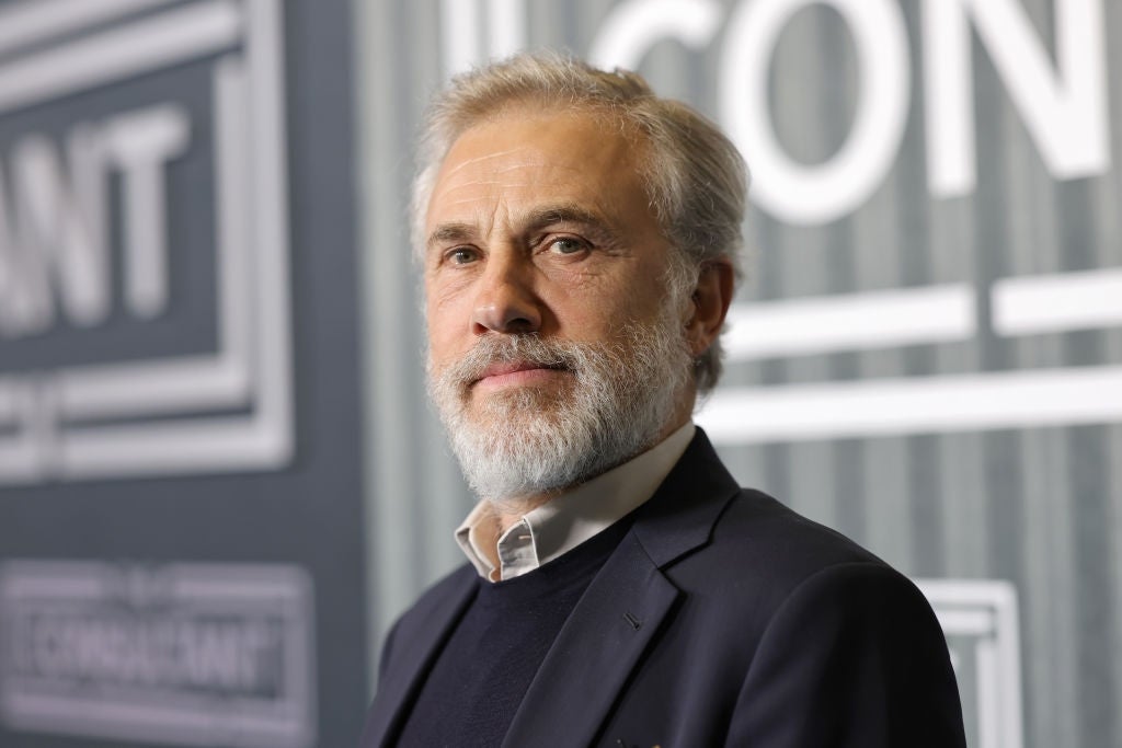 A idiosyncratic   with a abbreviated  grey  beard successful  a acheronian  suit   poses against a backdrop with graphic substance   astatine  a ceremonial  event