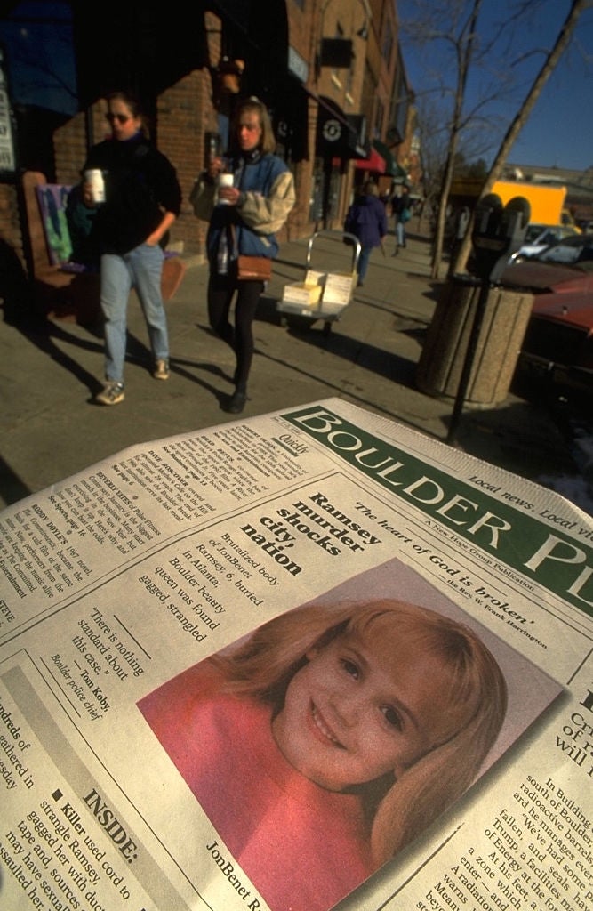 A newspaper headline about a murder case with an image of a young girl named JonBenét. People walk on a sidewalk, holding coffee cups