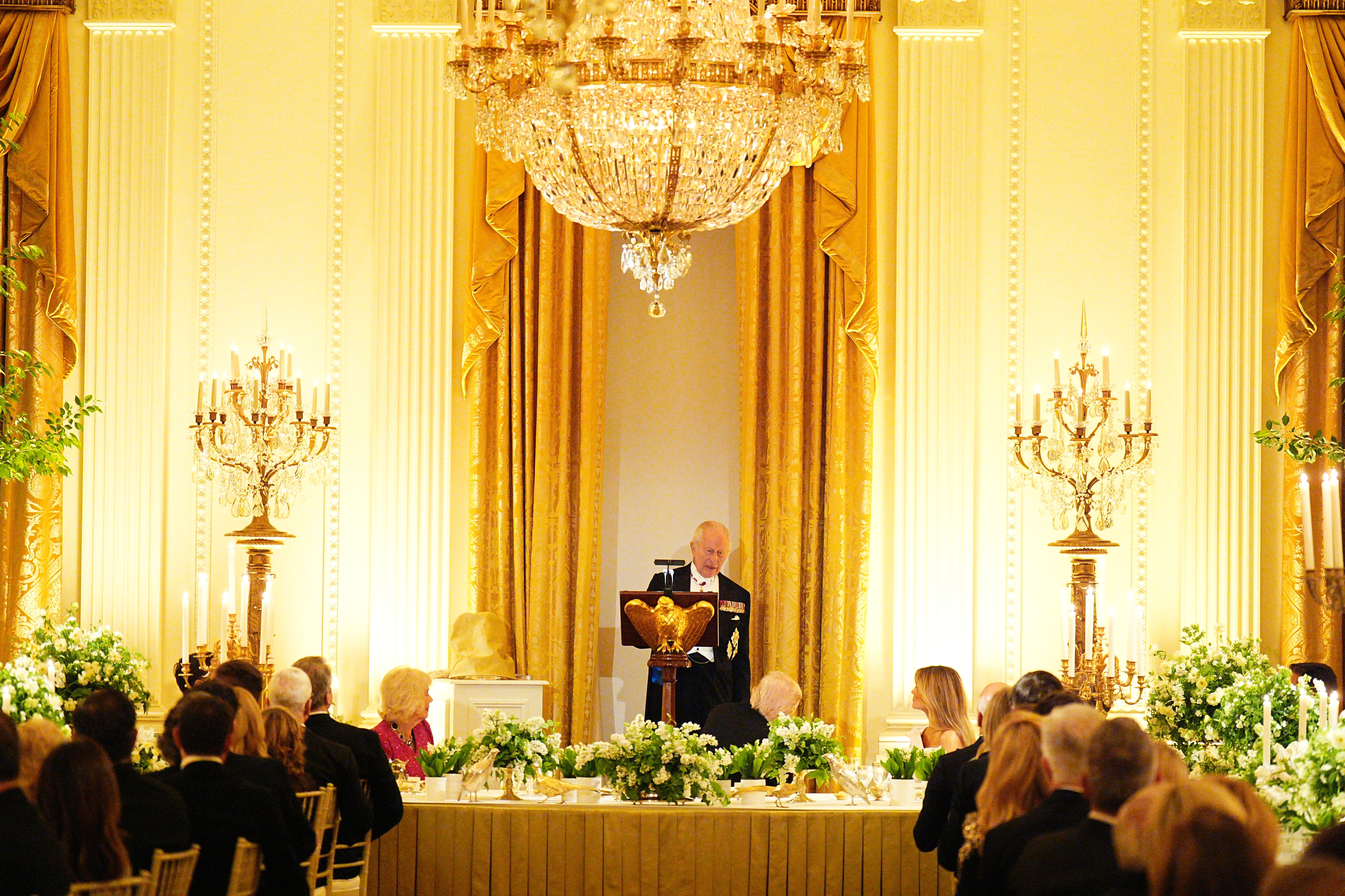 A ceremonial  meal  lawsuit   with a talker  astatine  a podium, elegant chandeliers, and guests seated astatine  decorated tables