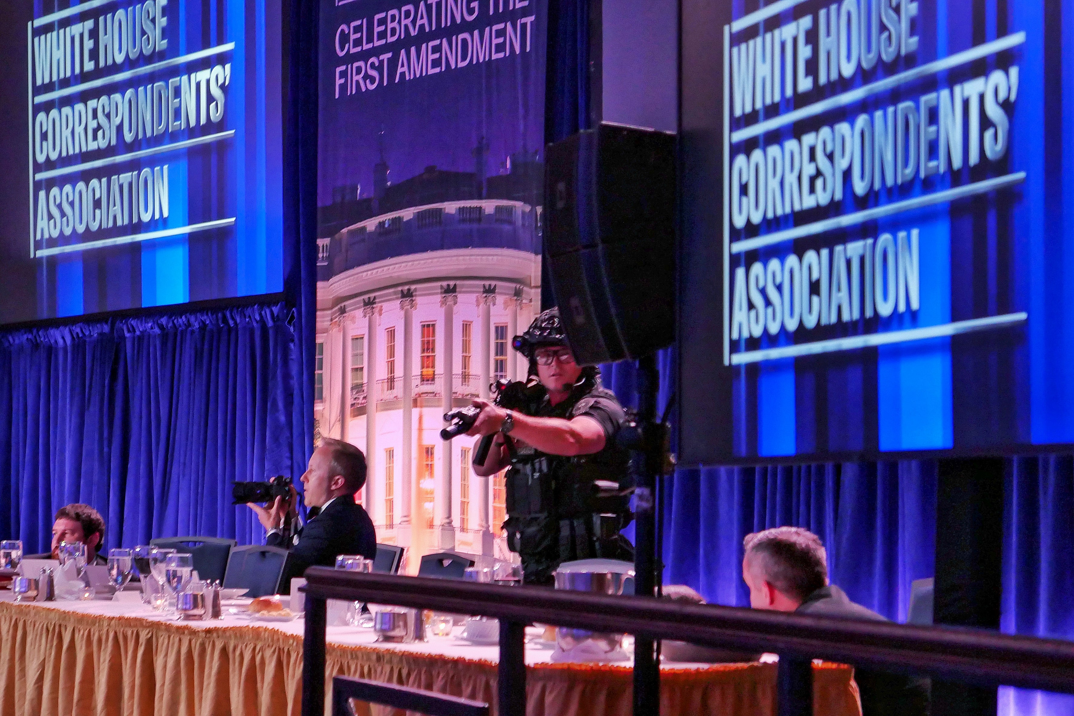 A lensman  and a information    serviceman  basal   by a banquet array  astatine  an lawsuit   with a backdrop of "White House Correspondents' Association" signs